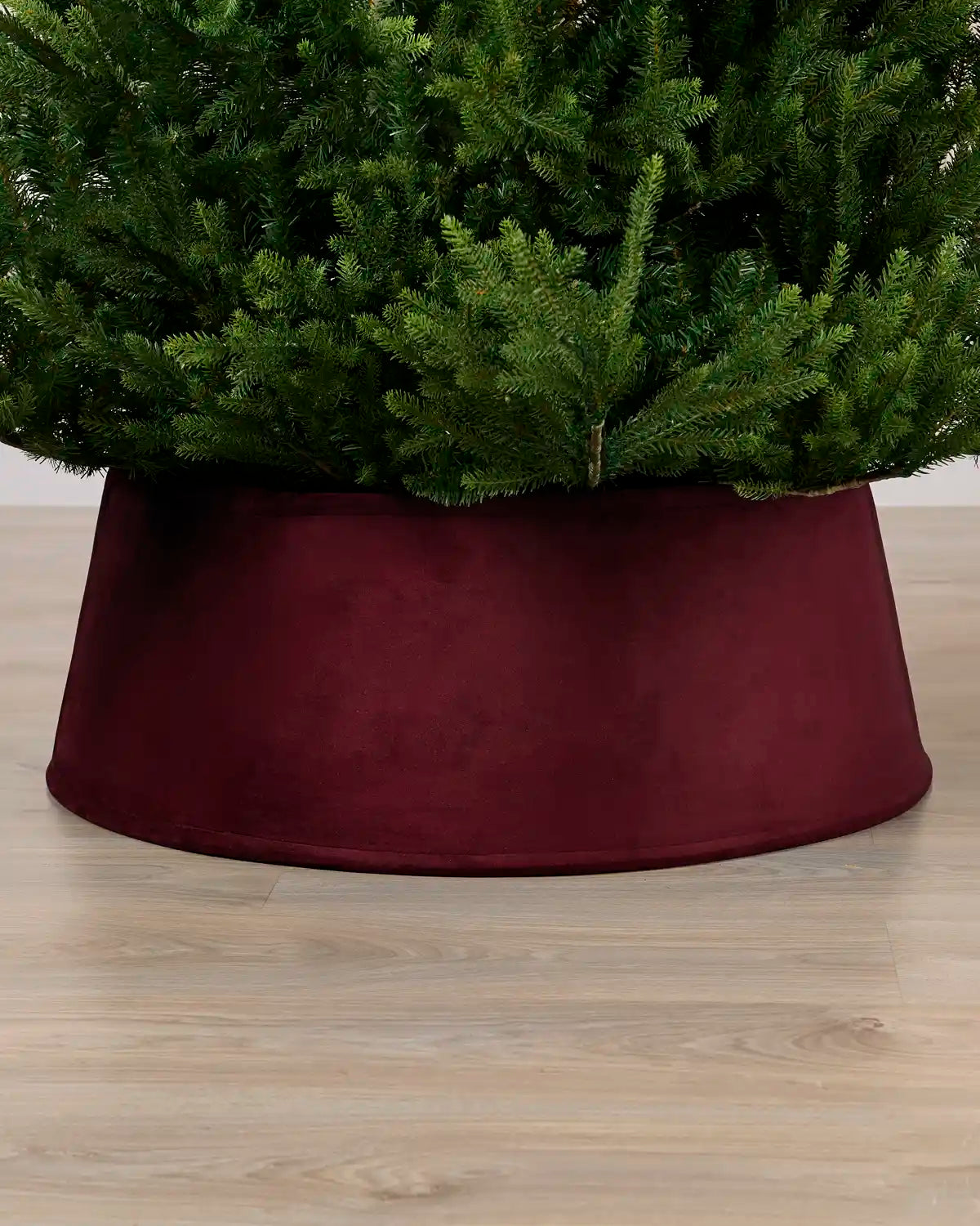 Burgundy coloured velvet tree skirt under a Christmas tree on a Light brown floor
