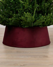 Burgundy coloured velvet tree skirt under a Christmas tree on a Light brown floor
