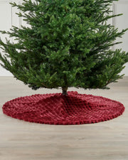 Burgundy diamond faux fur tree skirt on wooden flooring underneath a Christmas tree 