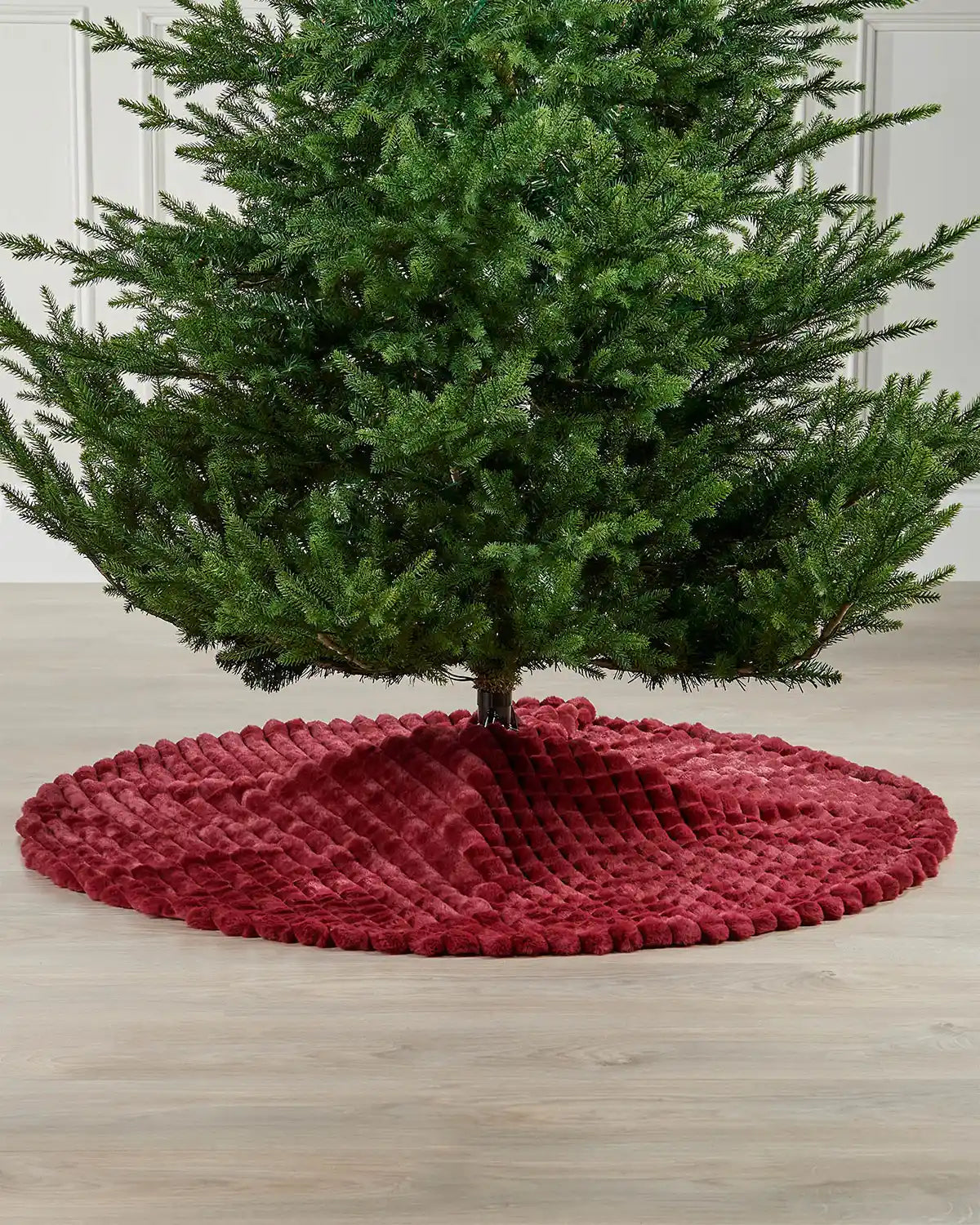 Burgundy diamond faux fur tree skirt on wooden flooring underneath a Christmas tree 