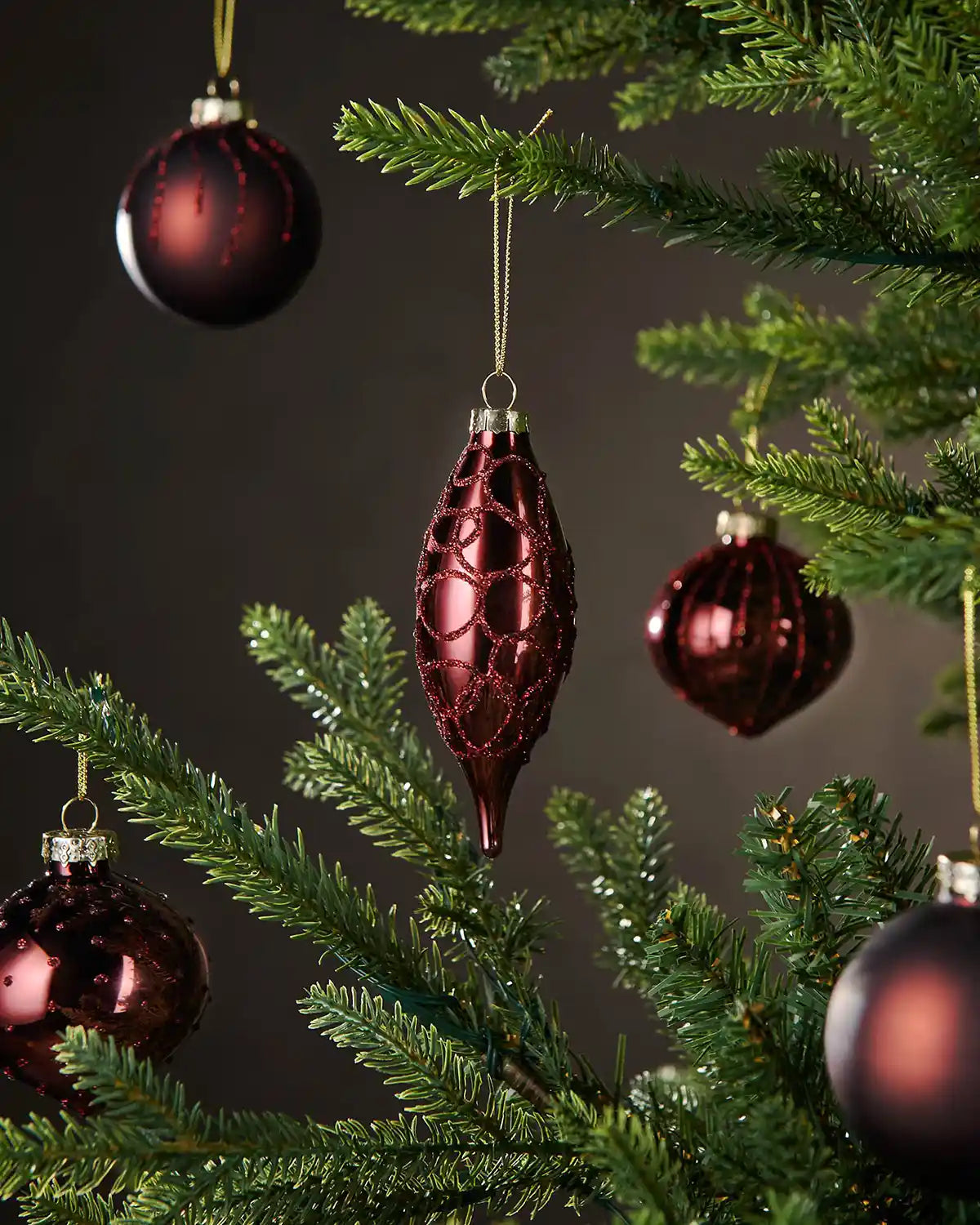 Burgundy glass ornaments on a Christmas tree with a dark background