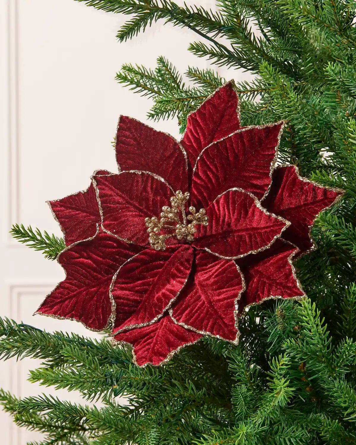 Burgundy glitter artificial poinsettia with gold-trimmed petals and a gold glitter berry center, displayed on a Christmas tree