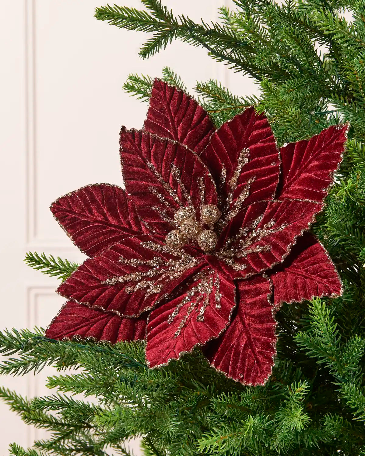 Burgundy glitter artificial poinsettia with layered velvet petals, gold sequin detailing, and gold glitter accents on a Christmas tree