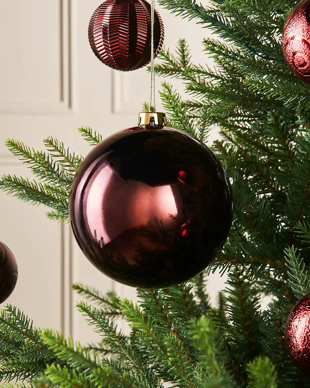 Burgundy gloss 15cm oversized bauble on a Christmas tree branch with 4 smaller burgundy baubles in background