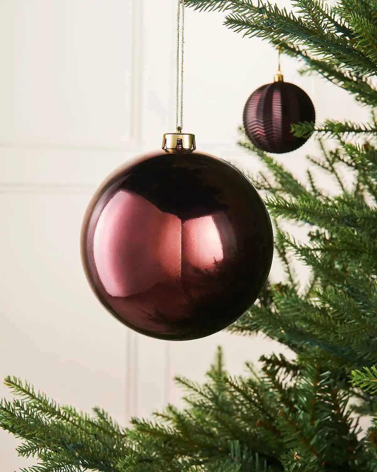 Burgundy gloss 15cm oversized bauble on a Christmas tree branch with a smaller burgundy bauble in background