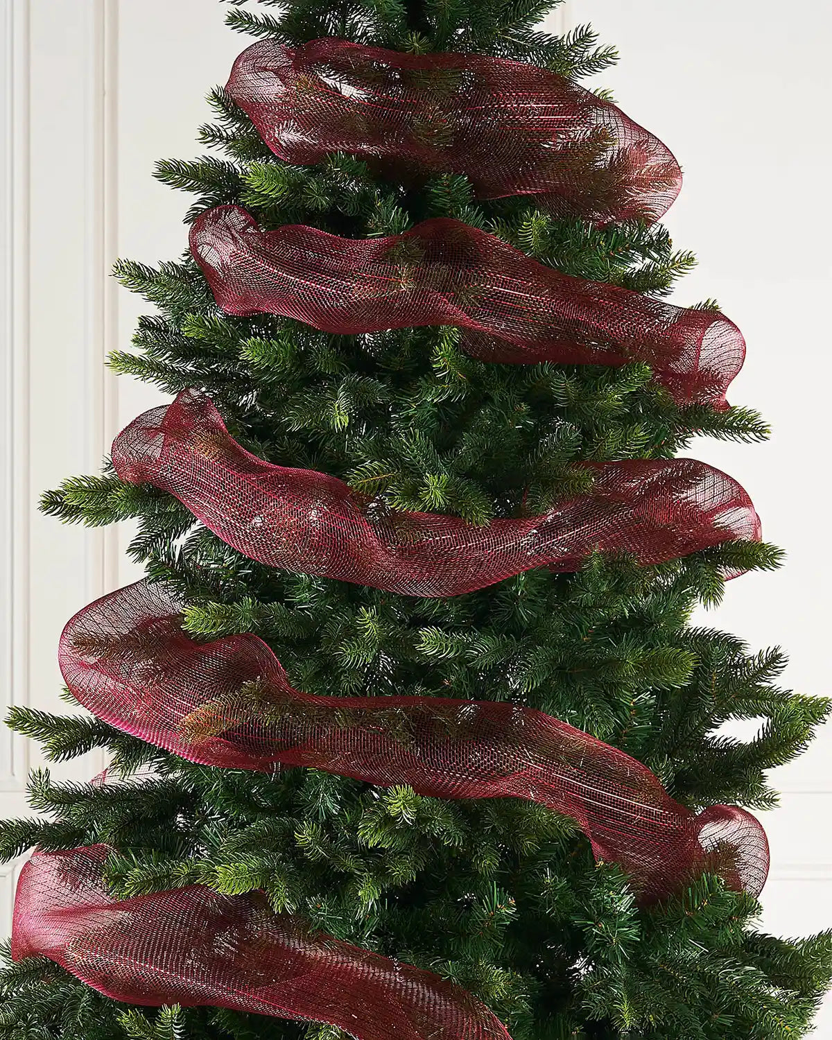 Burgundy mesh ribbon wrapped around Christmas tree against a cream panel wall