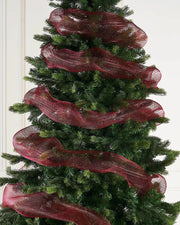 Burgundy mesh ribbon wrapped around Christmas tree against a cream panel wall