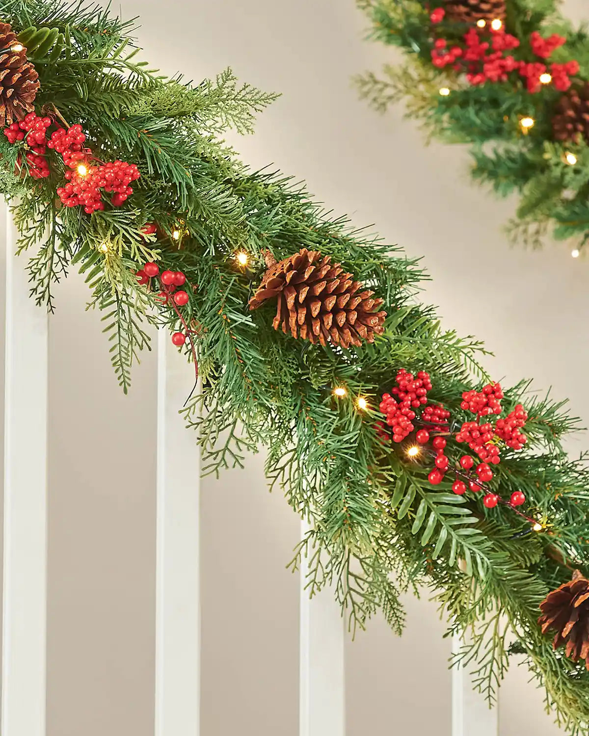 Christmas garland with greenery, red berries, and pinecones on a neutral background