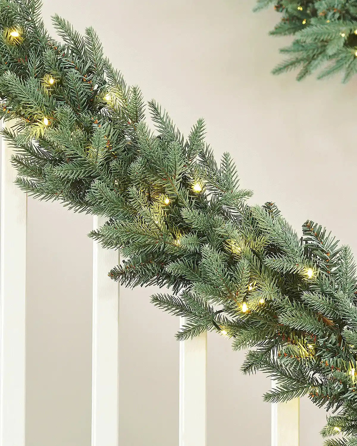 Christmas garland with warm white lights on a staircase banister against a cream wall