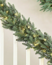 Christmas garland with warm white lights on a staircase banister against a cream wall