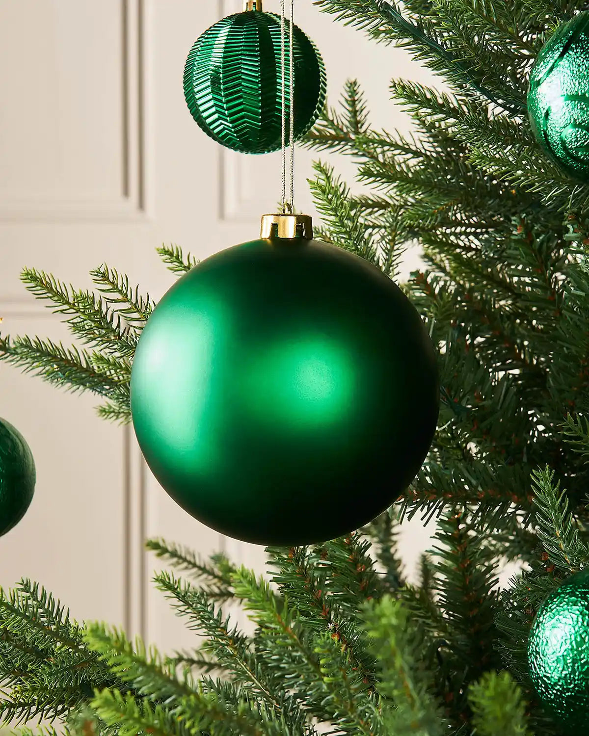 Christmas green oversized 15cm bauble on a Christmas tree branch with 4 smaller green baubles in background