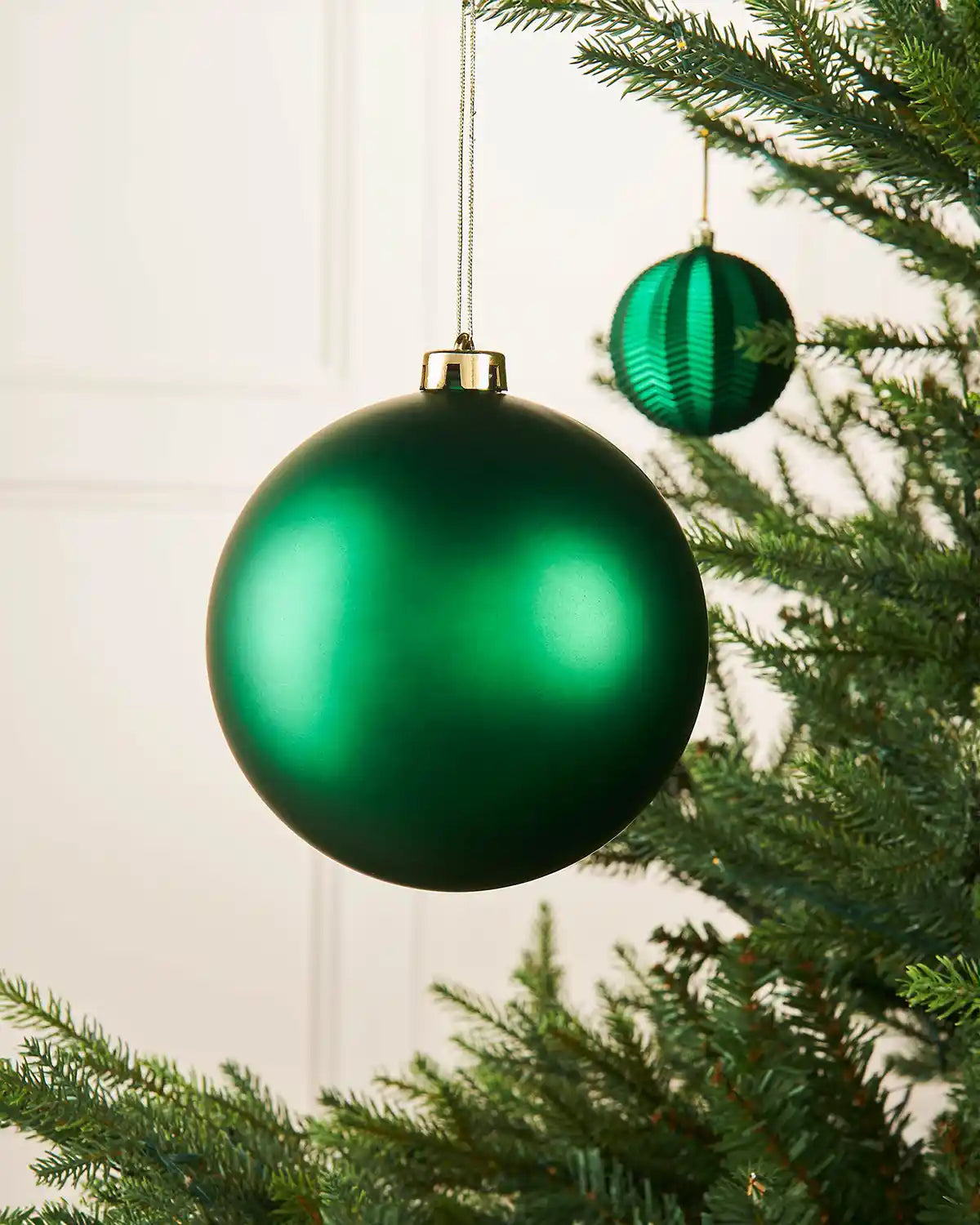 Christmas green oversized 15cm bauble on a Christmas tree branch with a smaller green bauble in background