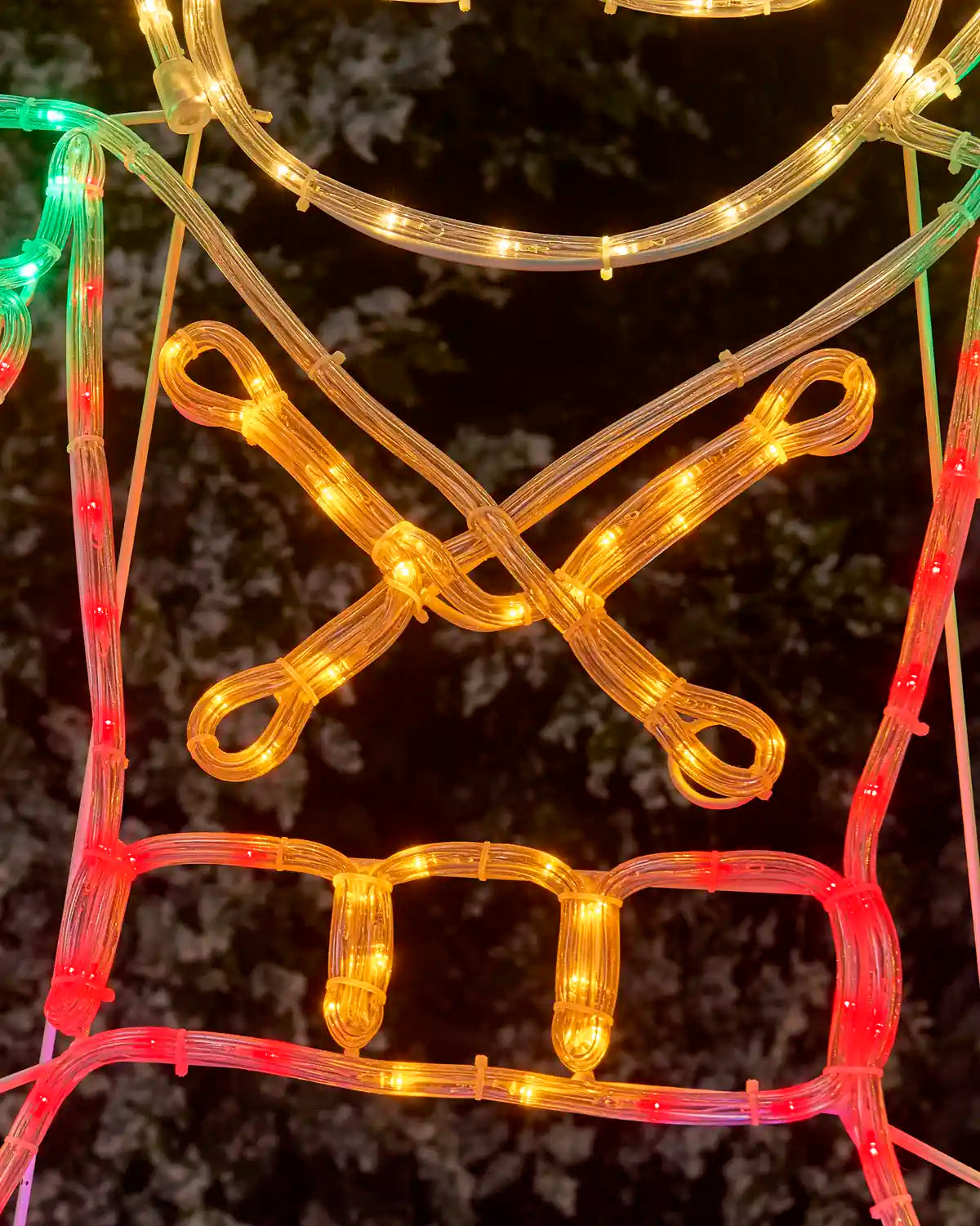 Christmas light decoration shaped like a nutcrackers shirt and belt, featuring warm white lights for the body and red and green accents, photographed outdoors against a dark, blurry background.