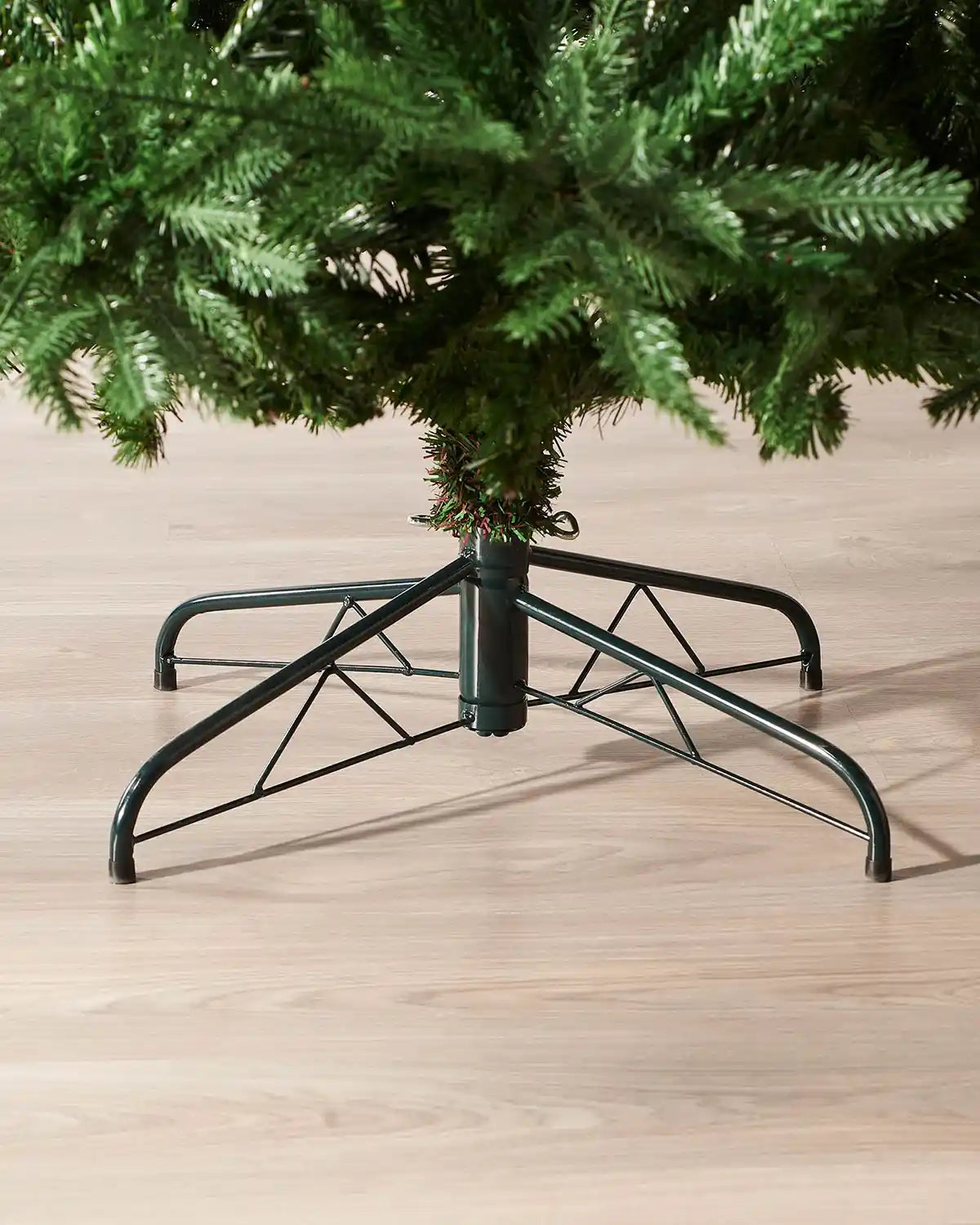 Christmas tree stand holding a green artificial Christmas tree on a wooden floor.