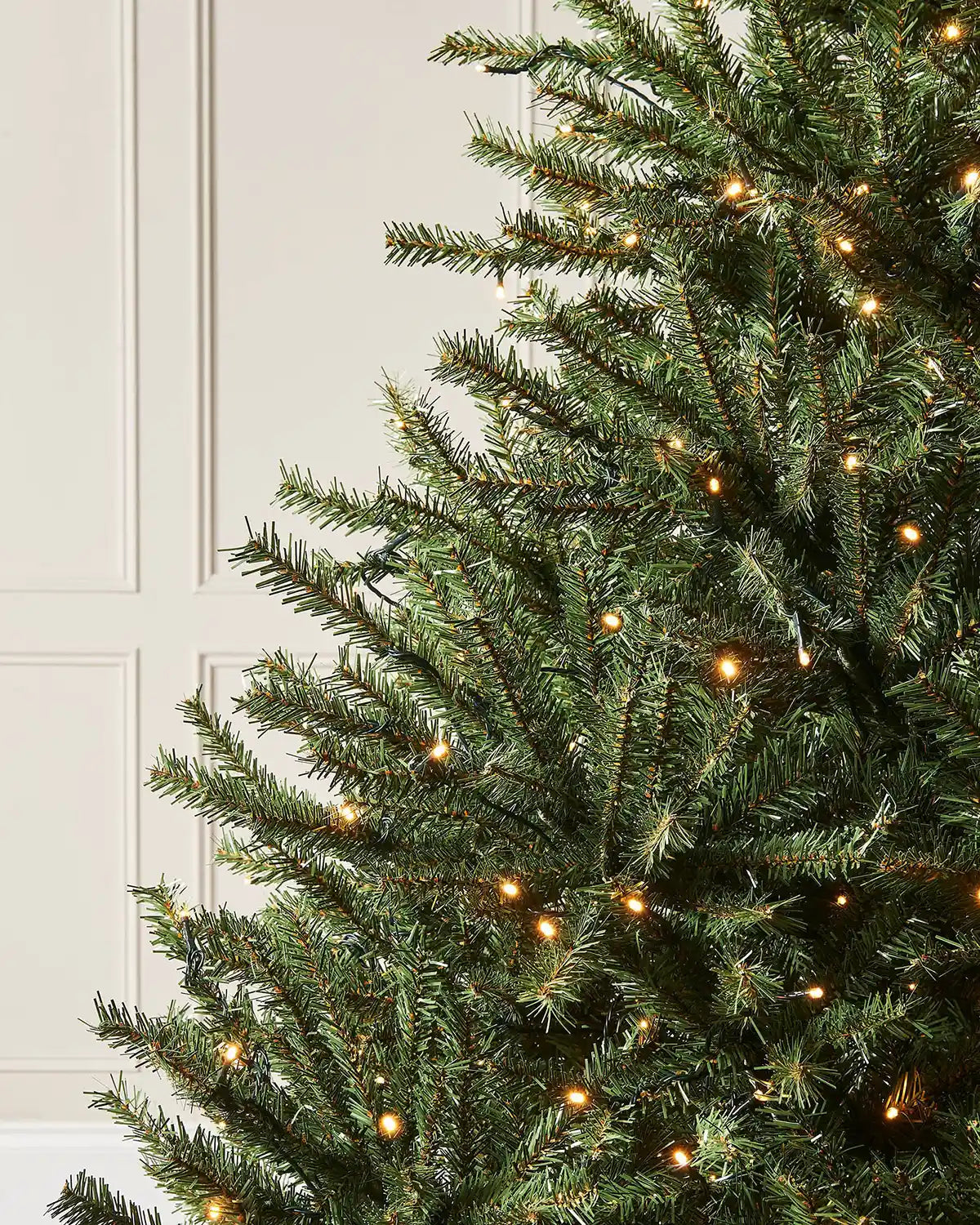 Christmas tree with lights and PVC and PE tips against a cream panel wall