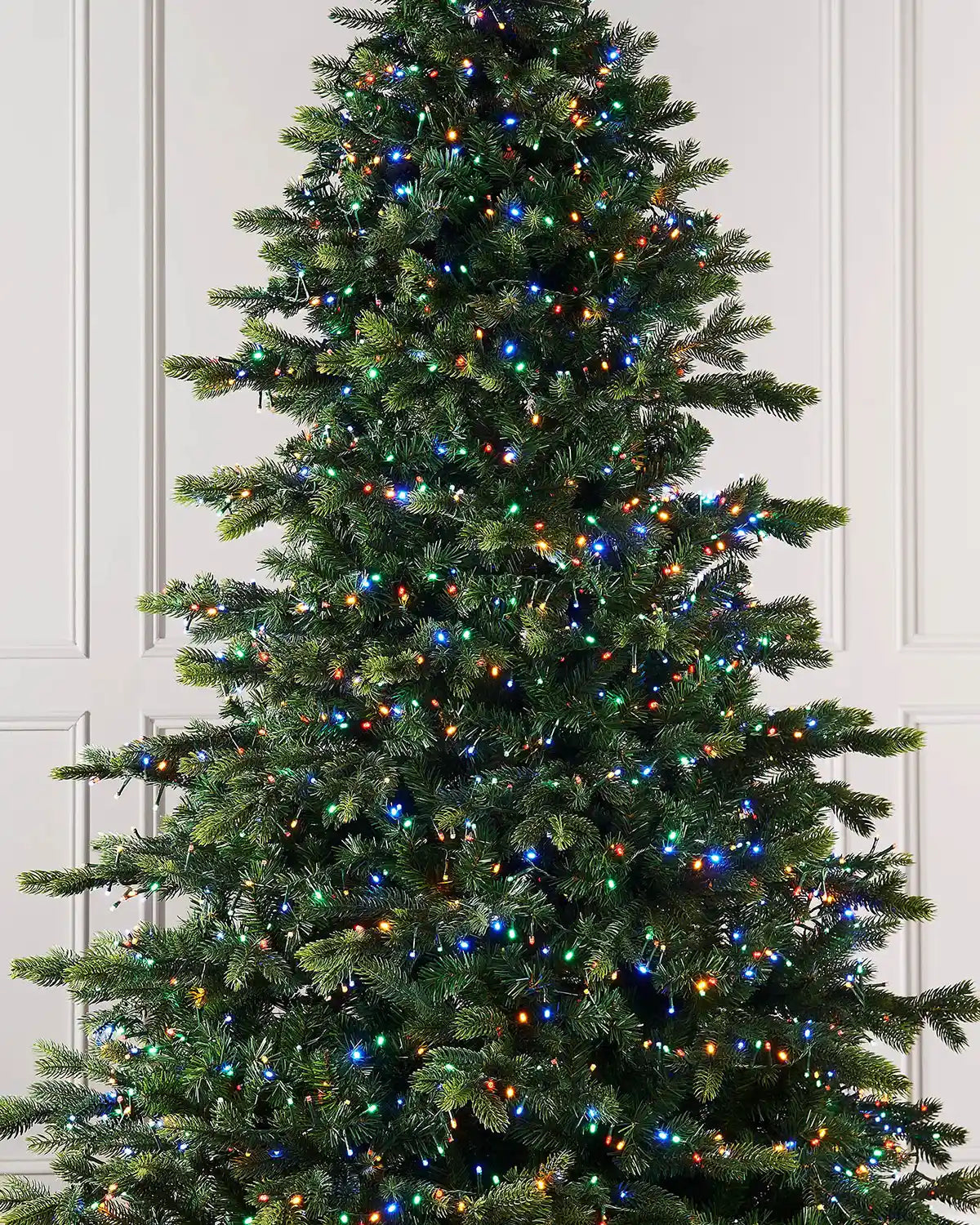 Christmas tree with multicoloured lights against a cream panel wall.
