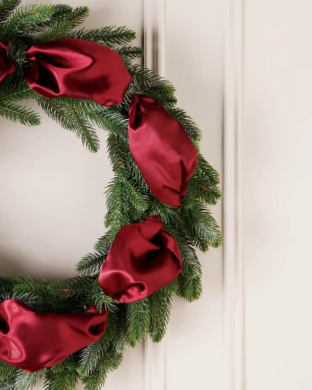 Christmas wreath with burgundy ribbons on a white wall