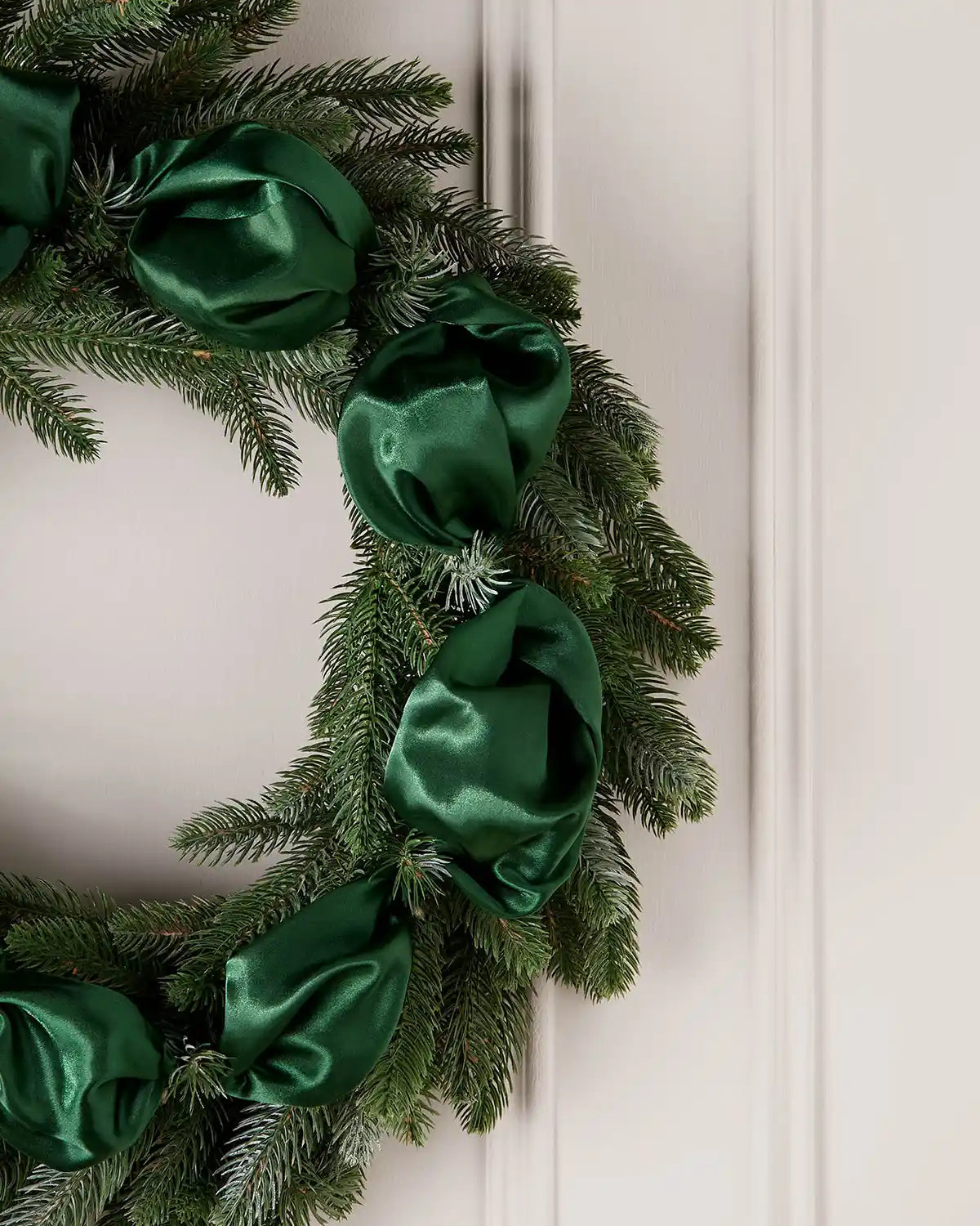 Christmas wreath with green ribbons on a white door