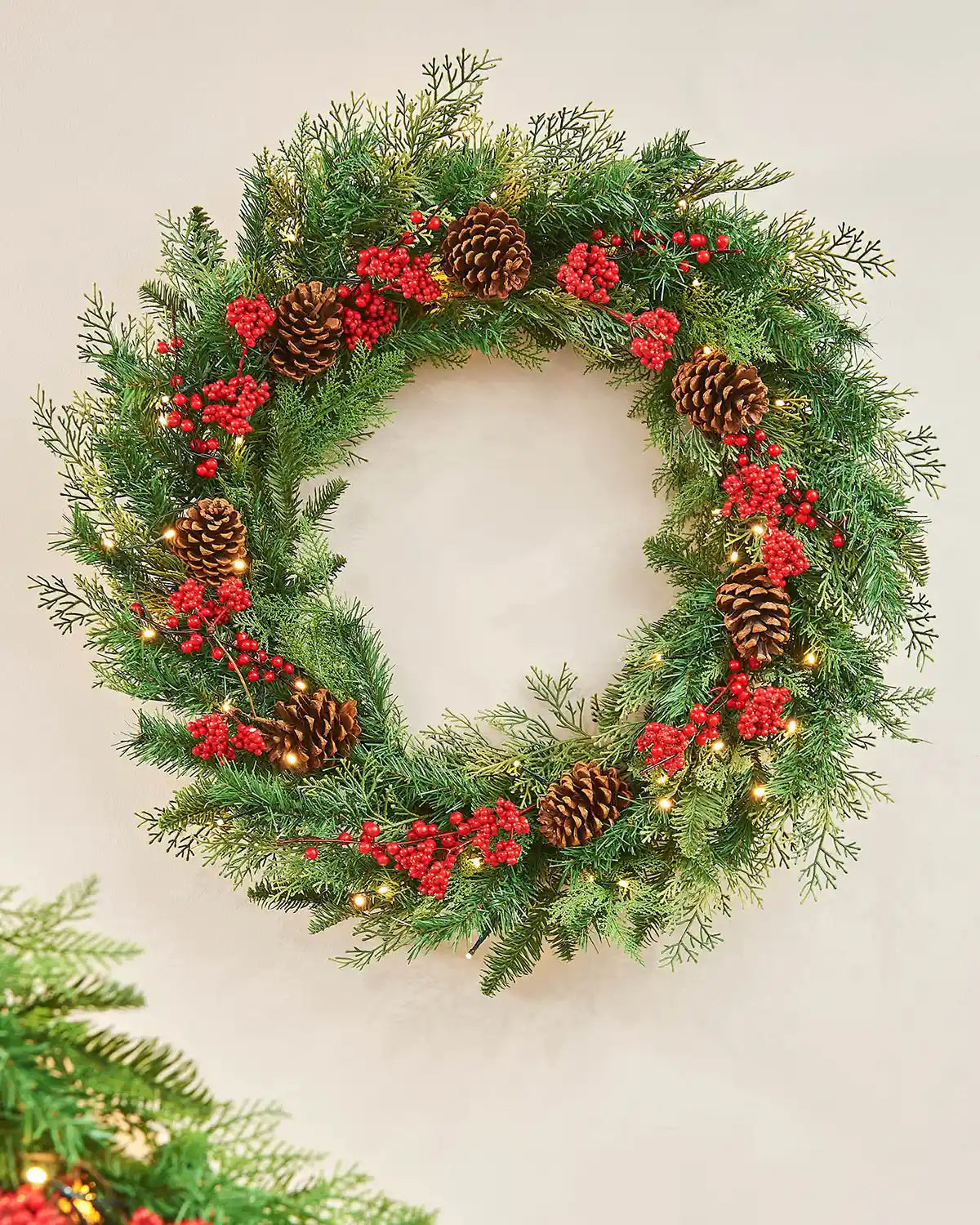 Christmas wreath with greenery, red berries, and pinecones on a light background