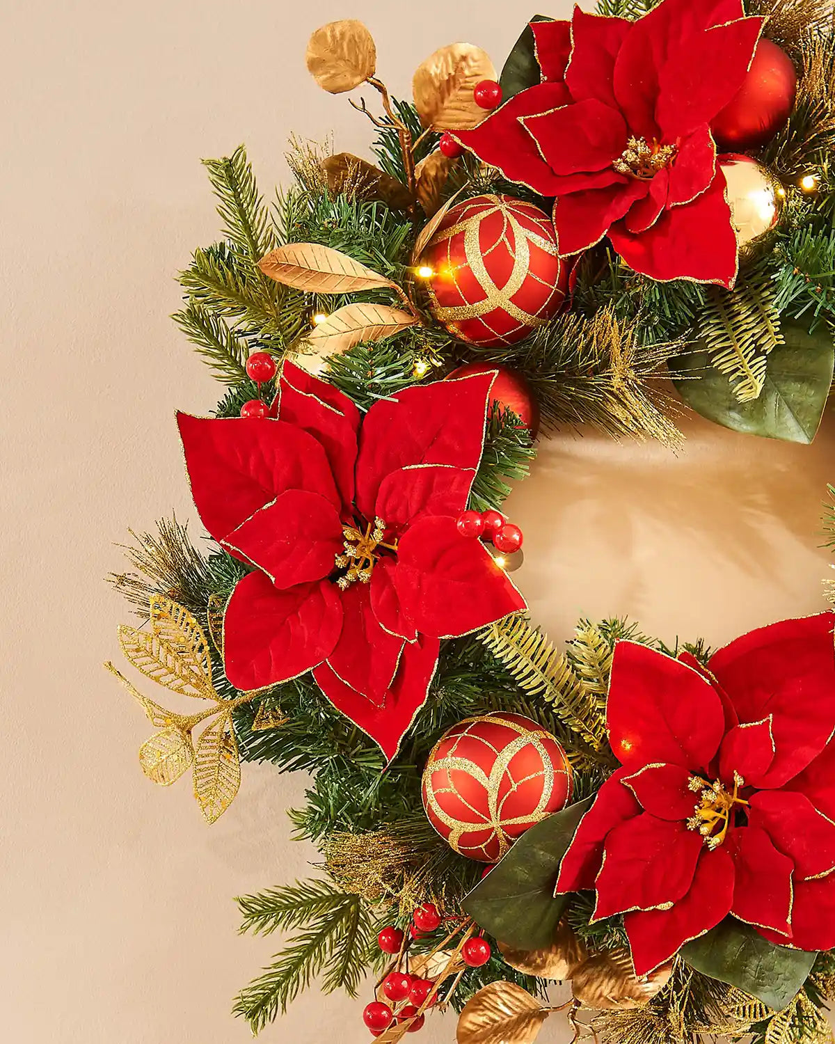 Christmas wreath with red poinsettias and gold leaves on a beige background