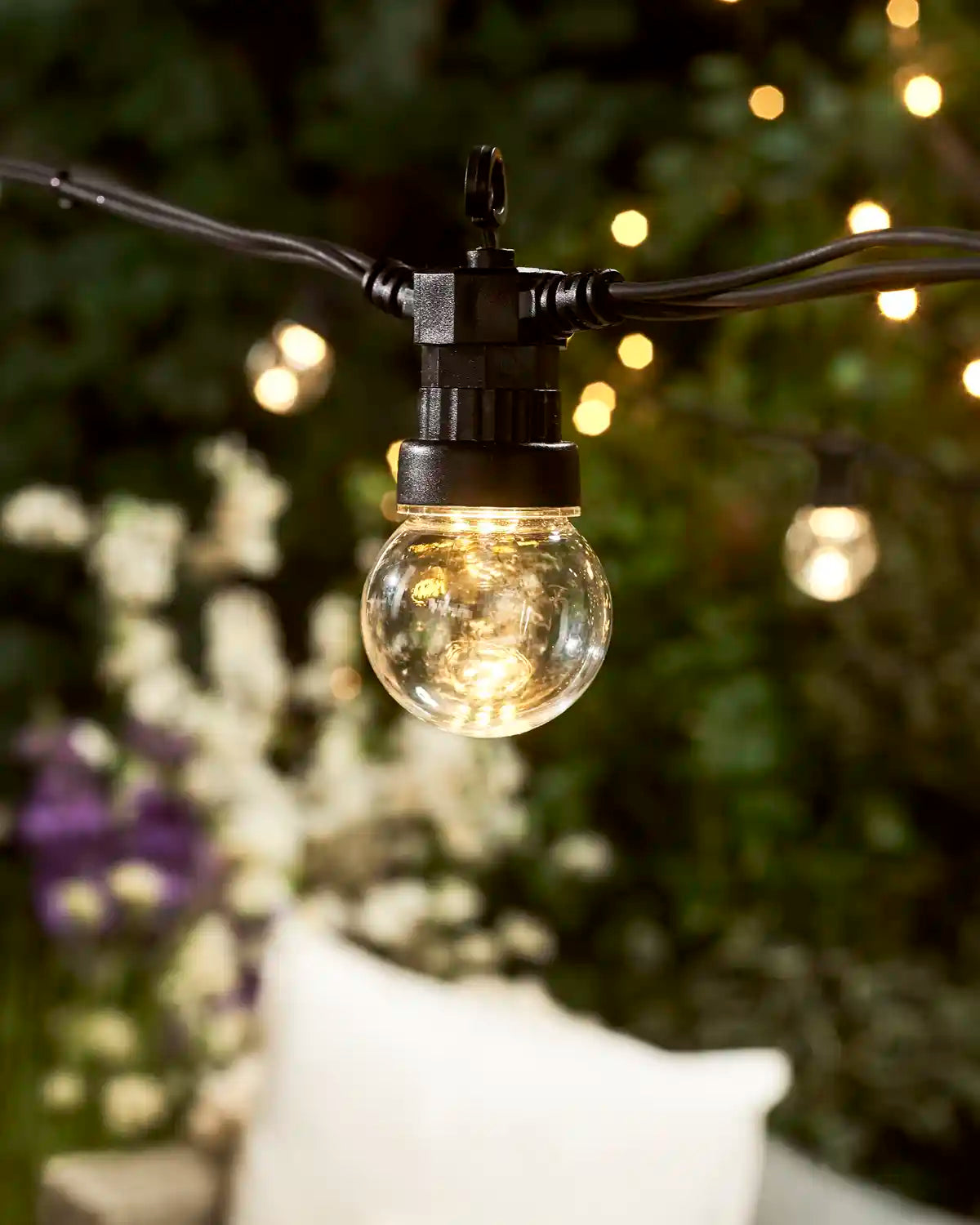 Close-up of a warm white festoon string light with a black connectable cable and garden background