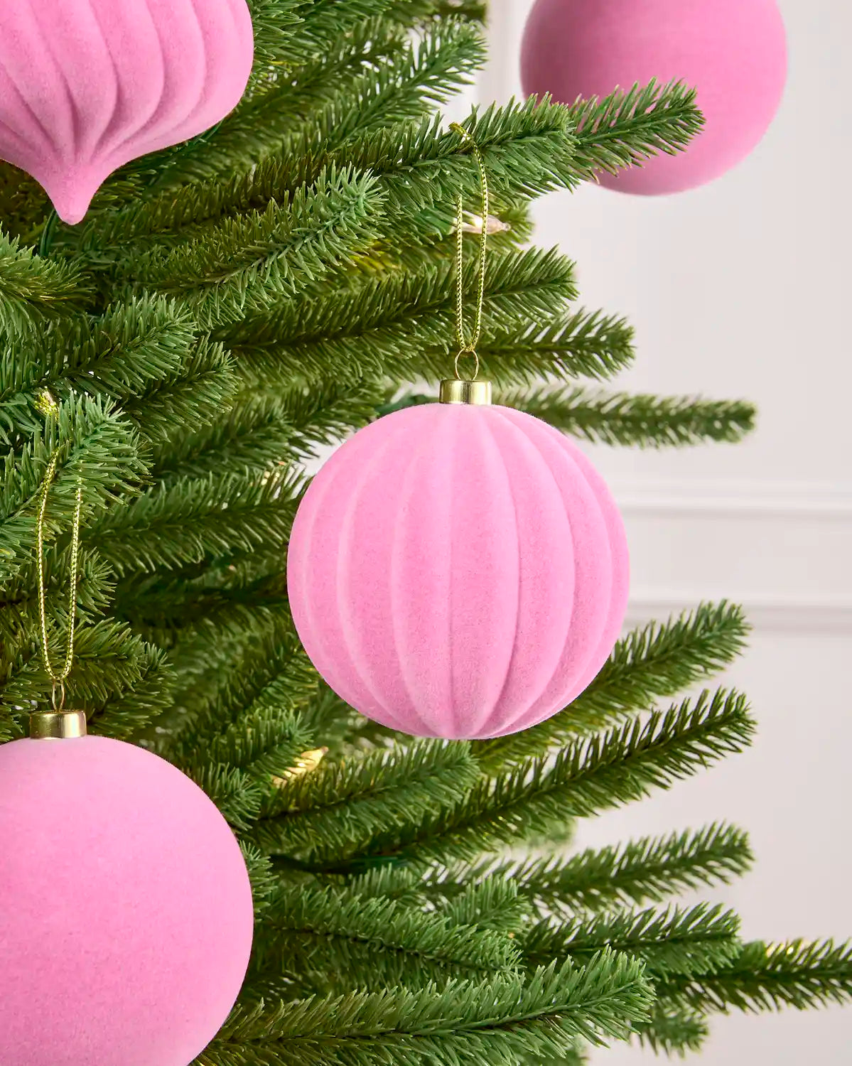 Close-up Pink velvet round swirl bauble hanging from Christmas tree branch with other pink velvet baubles hanging in the background