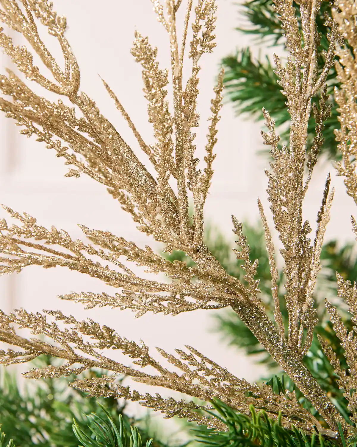 Close-up gold glitter tree spray showing the gold glitter detailing with blurry cream background