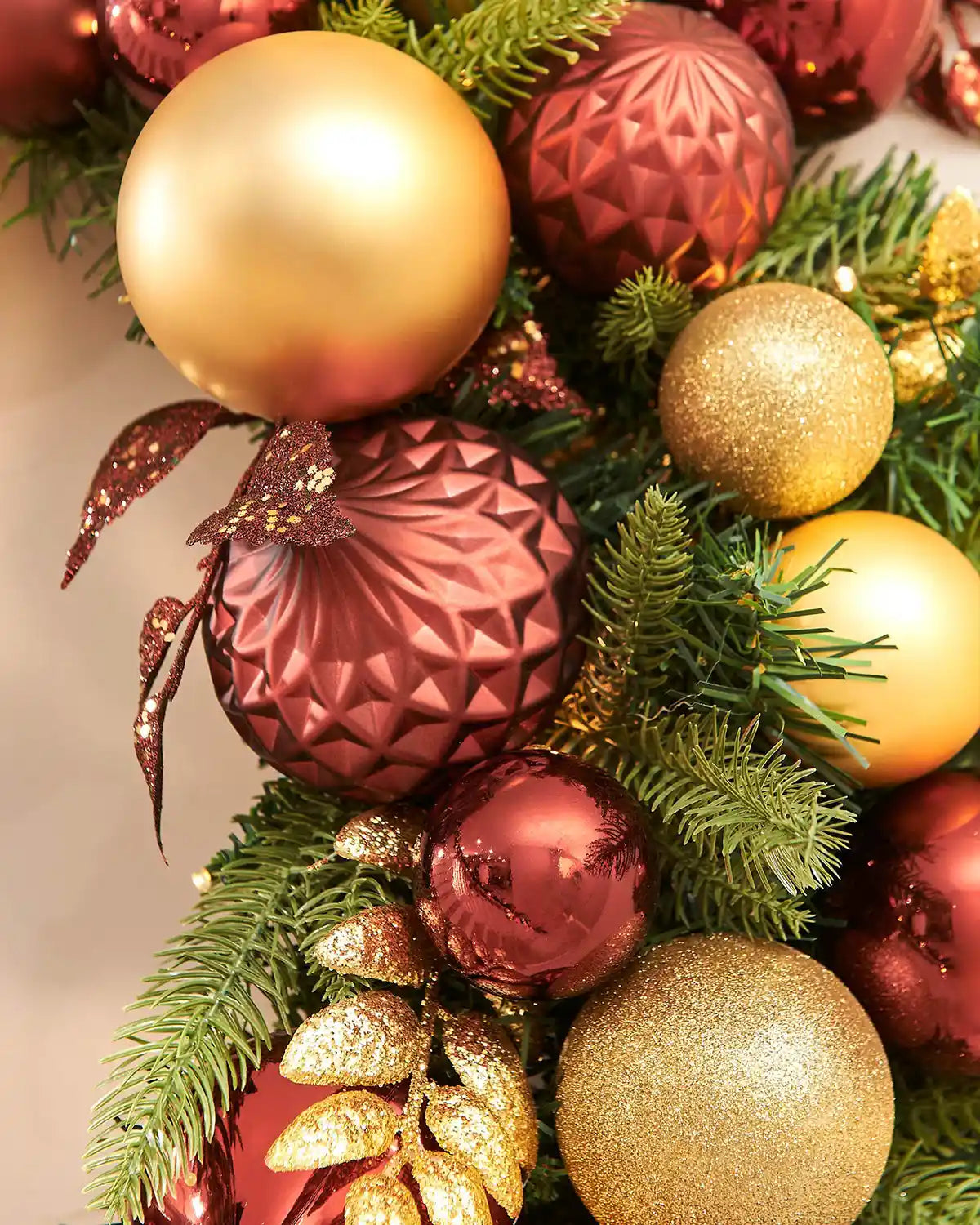 Close-up of Christmas ornaments including gold and burgundy baubles on a green wreath.