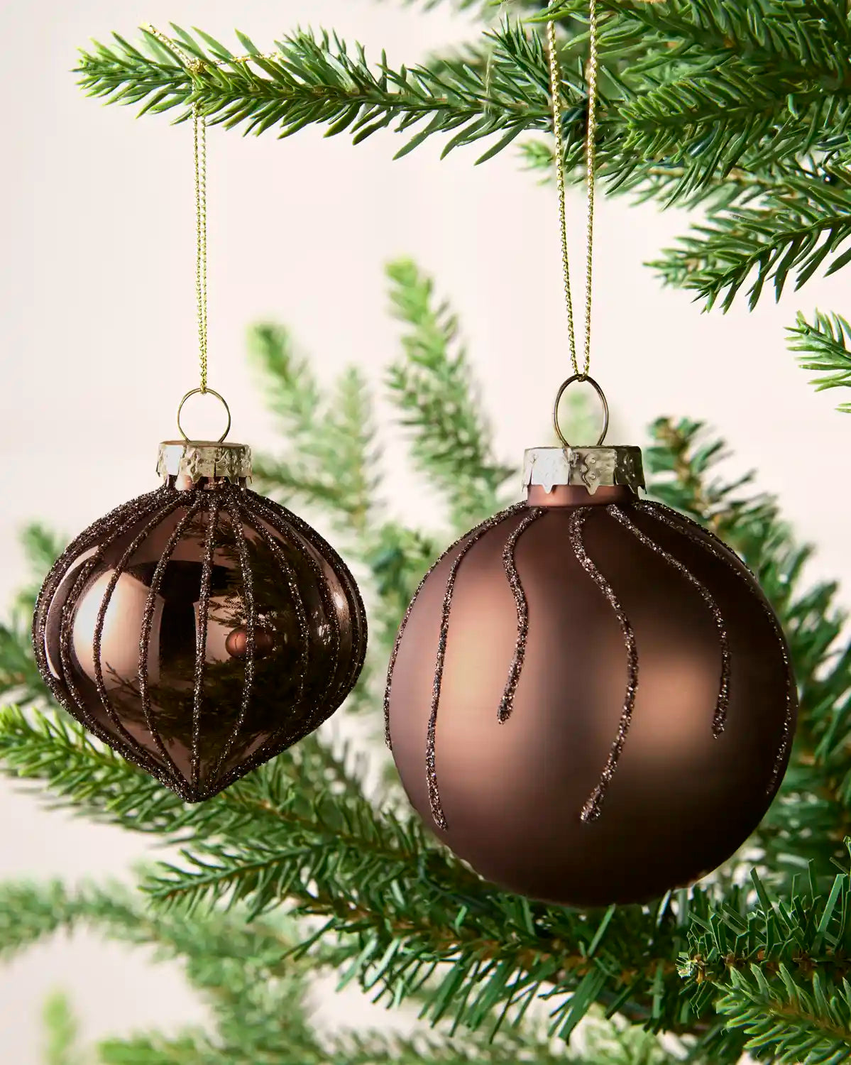 Close-up of Espresso onion-shaped and round glass baubles with glitter stripe patterns.
