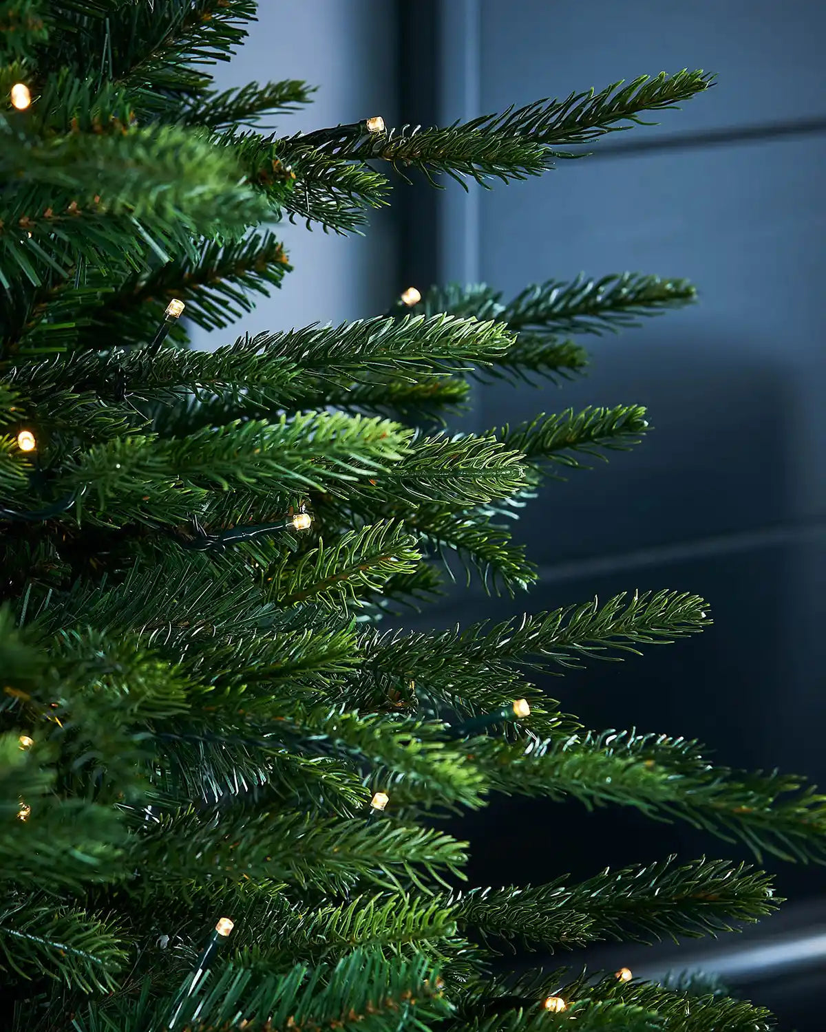 Close-up of PVC and PE tips of Decorated Pre-Lit Grand Fir Potted Christmas Tree with single lit warm white lights in a textured black pot 