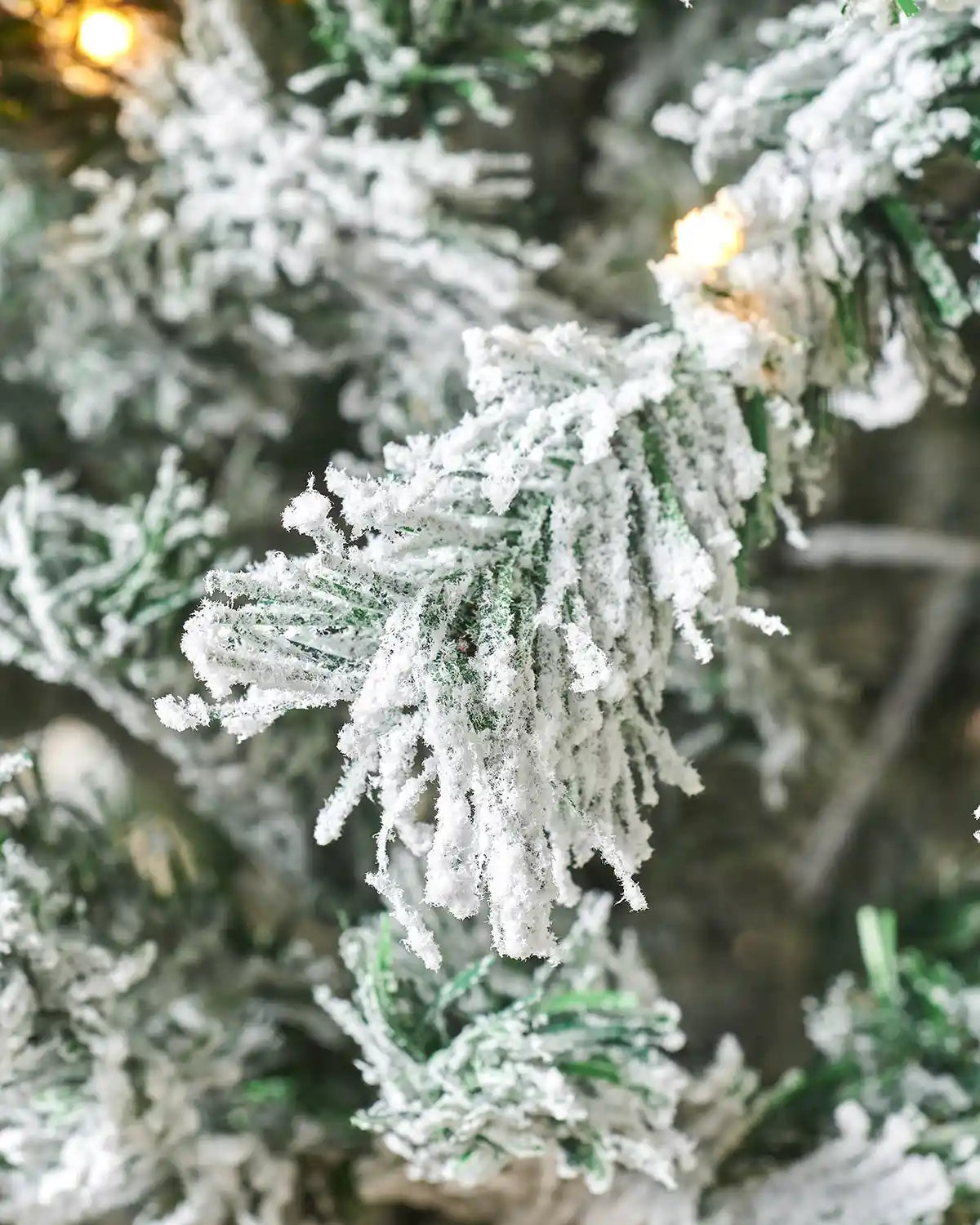 Close-up of a 7ft snow flocked Christmas tree with warm white lights and PVC and PE tips 