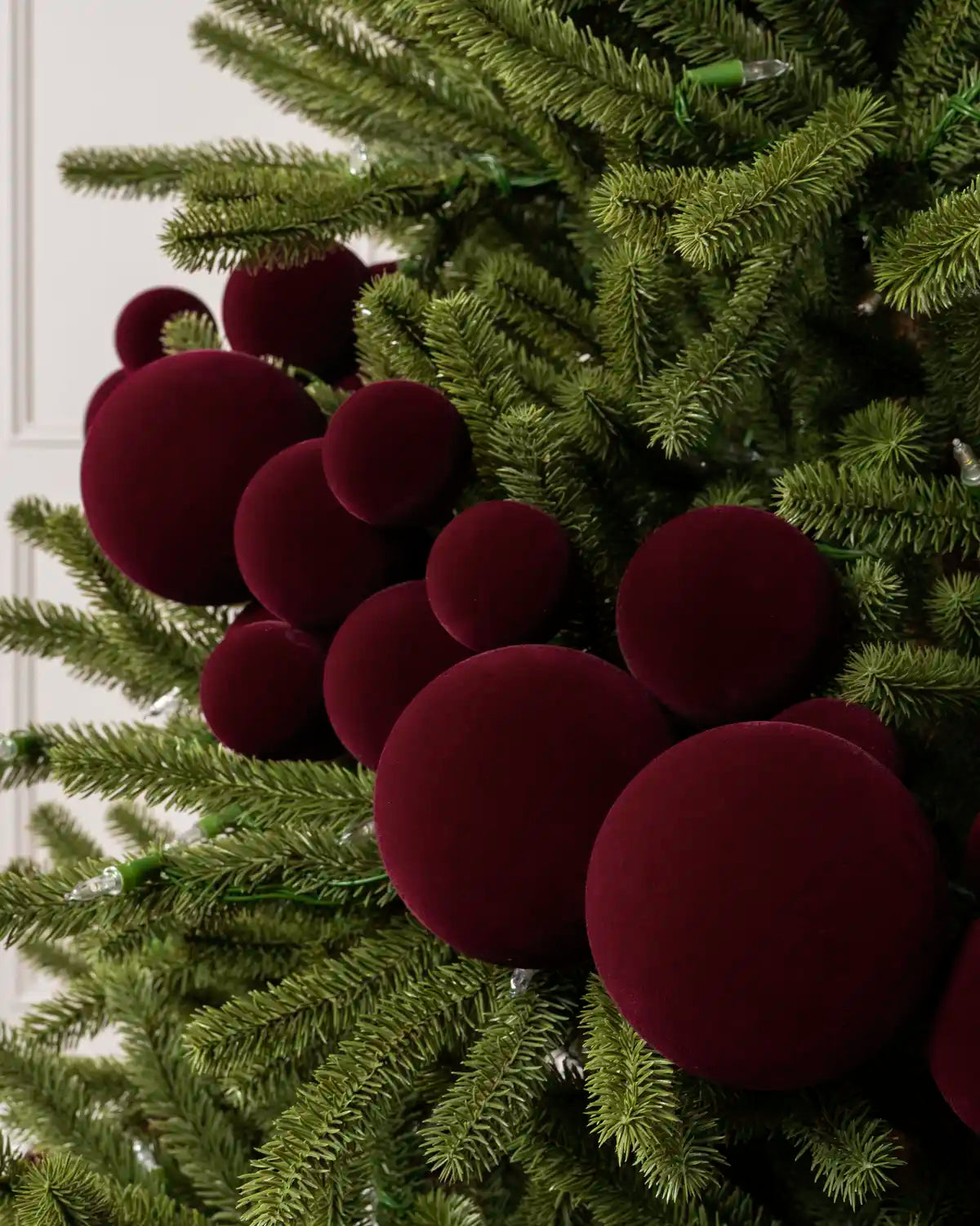 Close-up of a Burgundy Velvet Bauble Garland on a Christmas tree, featuring soft burgundy velvet baubles.