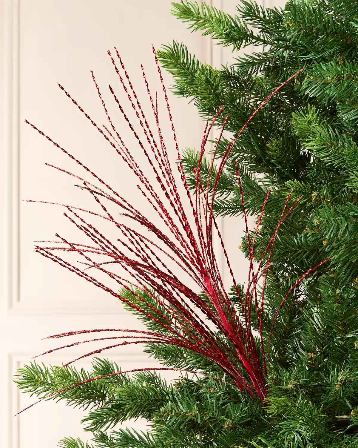Close-up of a Christmas tree decorated with a red glitter fountain spray featuring long, twisting metallic strands.
