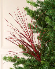Close-up of a Christmas tree decorated with a red glitter fountain spray featuring long, twisting metallic strands.

