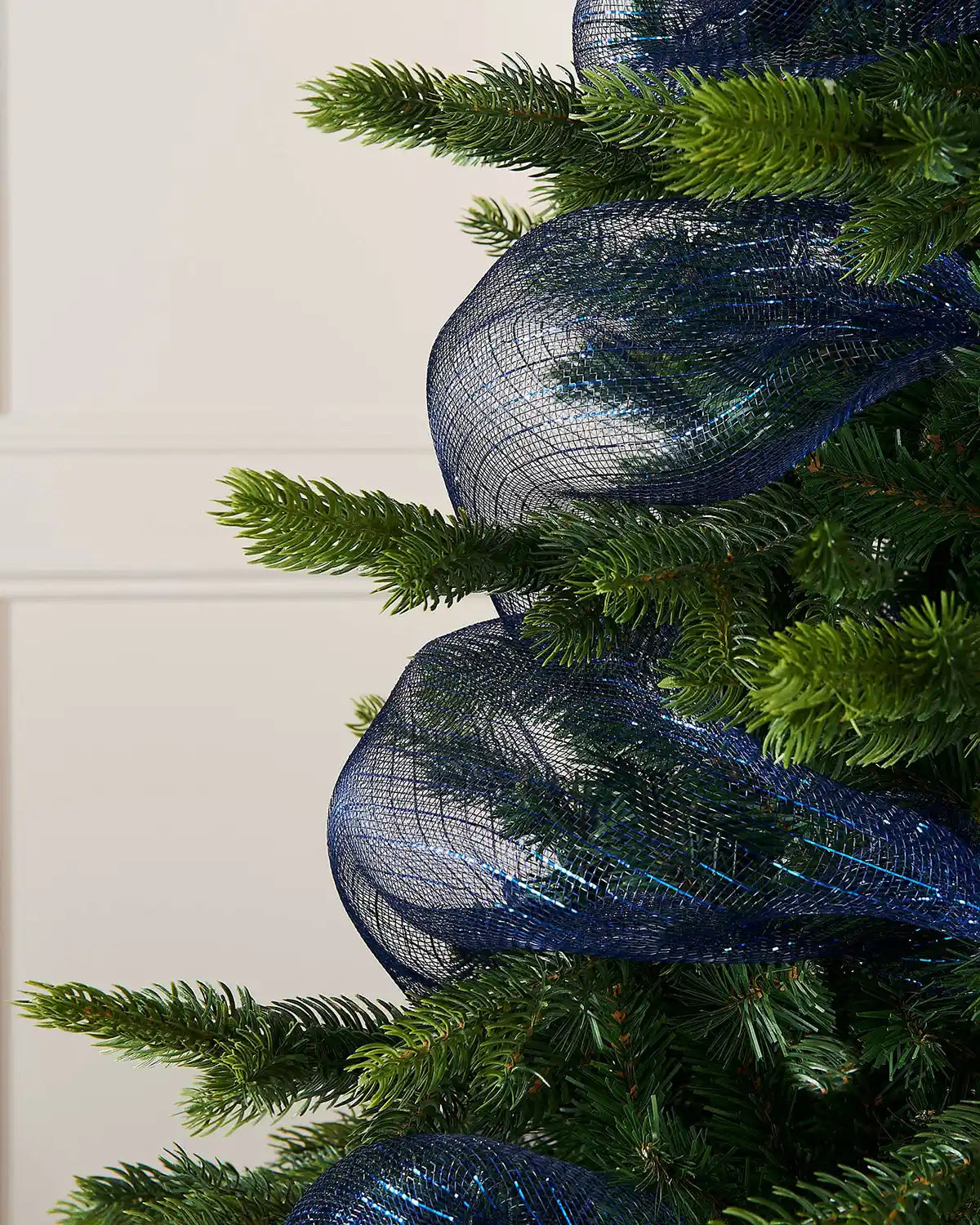 Close-up of a Christmas tree with blue mesh ribbon against a white wall