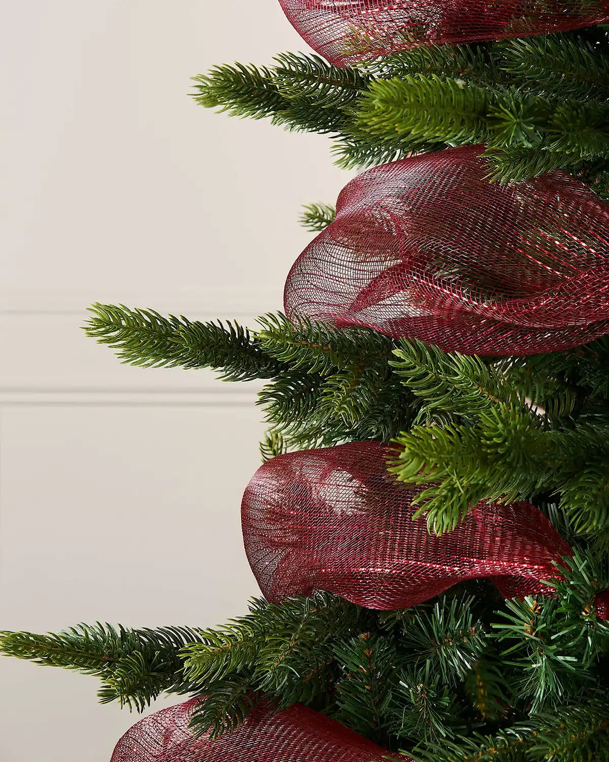 Close-up of a Christmas tree with burgundy ribbon against a white wall
