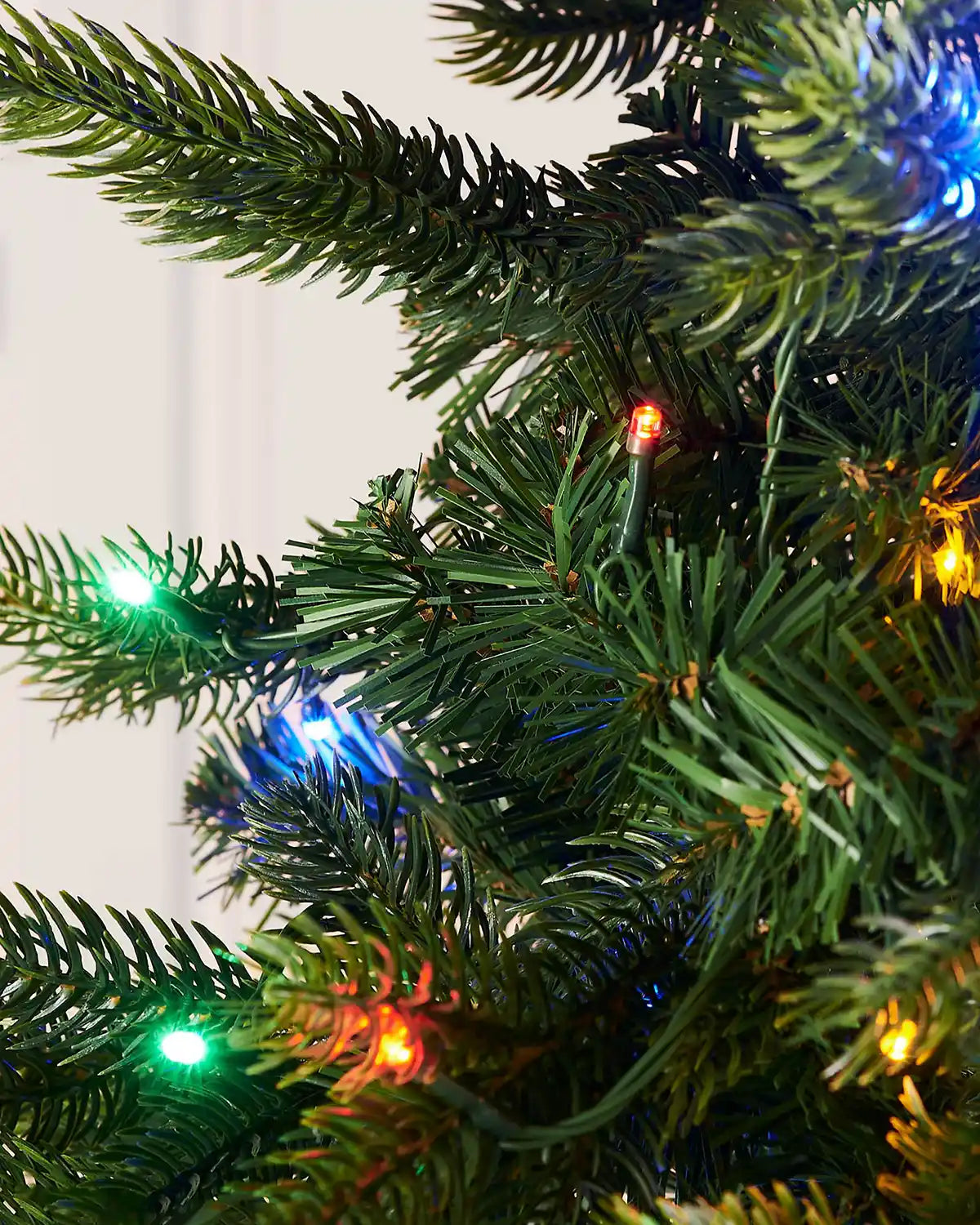 Close-up of a Christmas tree with colourful lights on a plain background