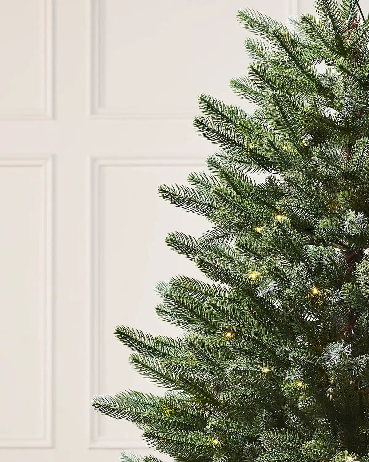 Close-up of a Christmas tree with lights against a cream wall.