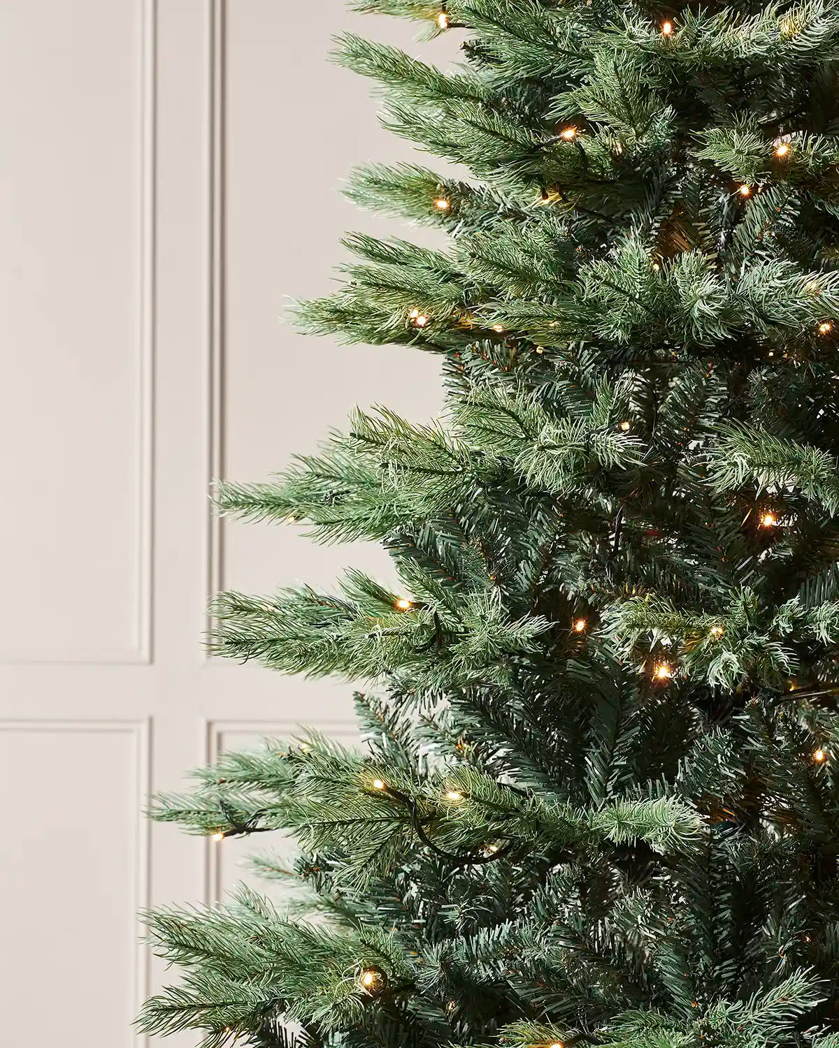 Close-up of a Christmas tree with lights against a white wall.