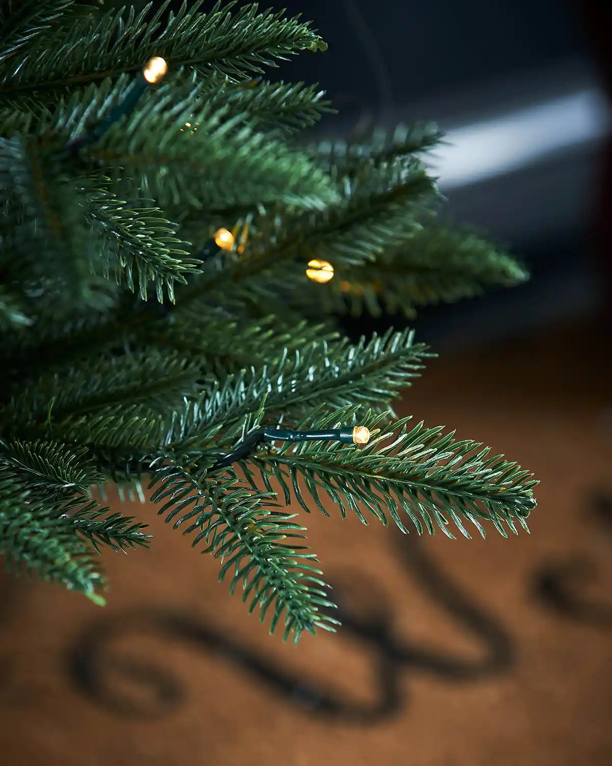 Close-up of a Christmas tree with lights on a blurred background with a doormat 