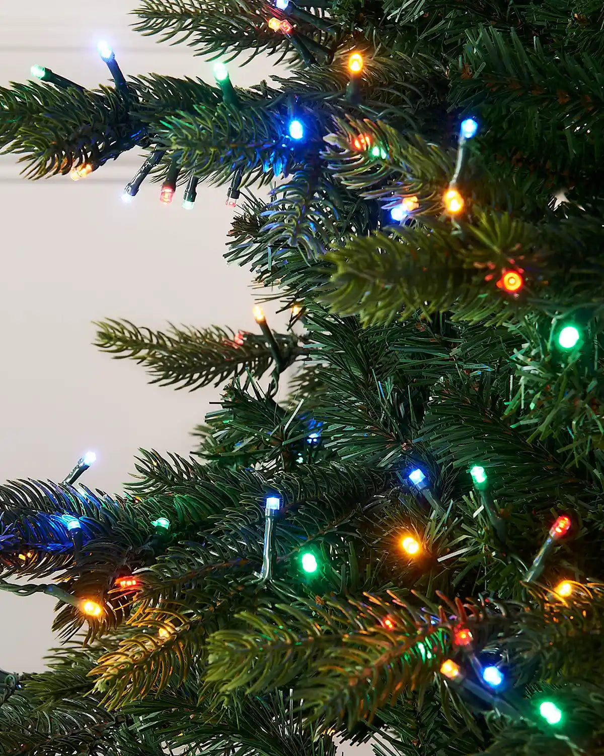 Close-up of a Christmas tree with multicoloured lights on a plain background