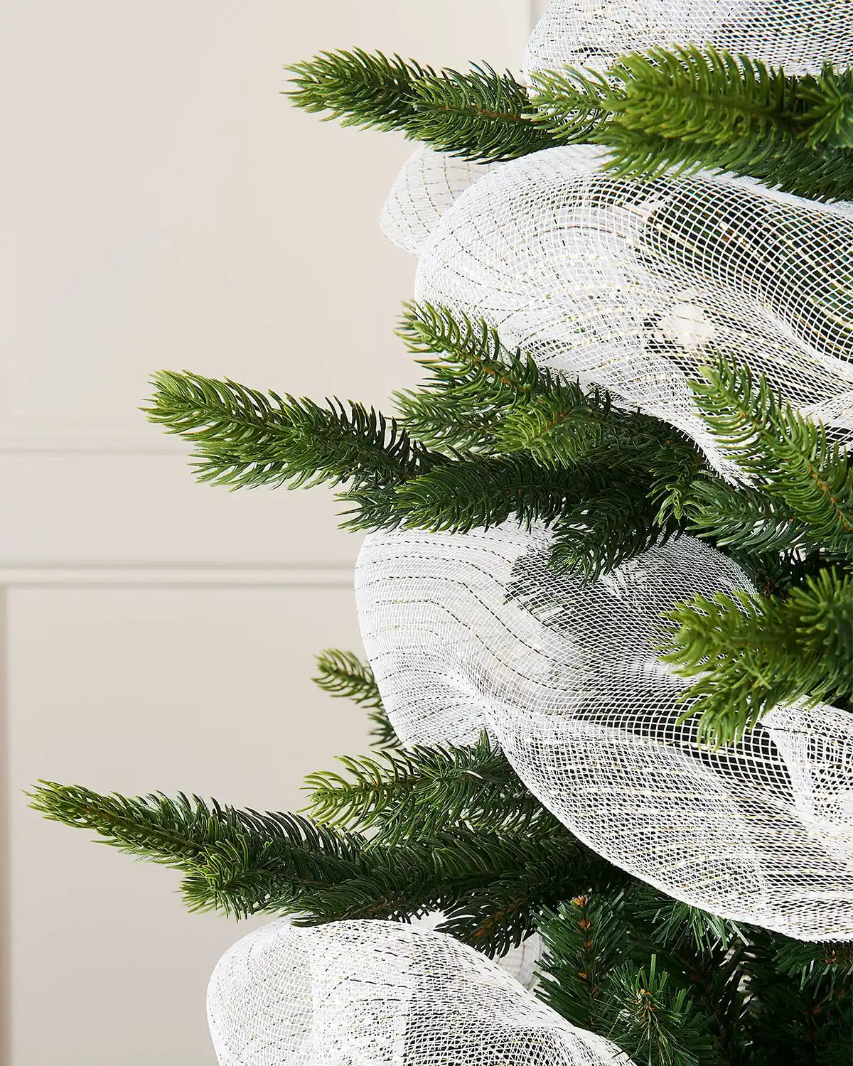 Close-up of a Christmas tree with white and gold mesh ribbon against a neutral background