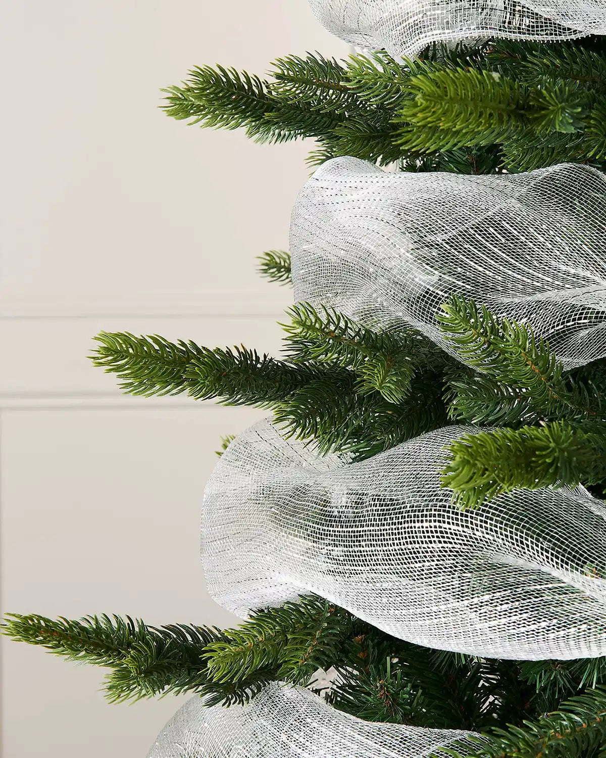 Close-up of a Christmas tree with white mesh ribbon against a neutral background