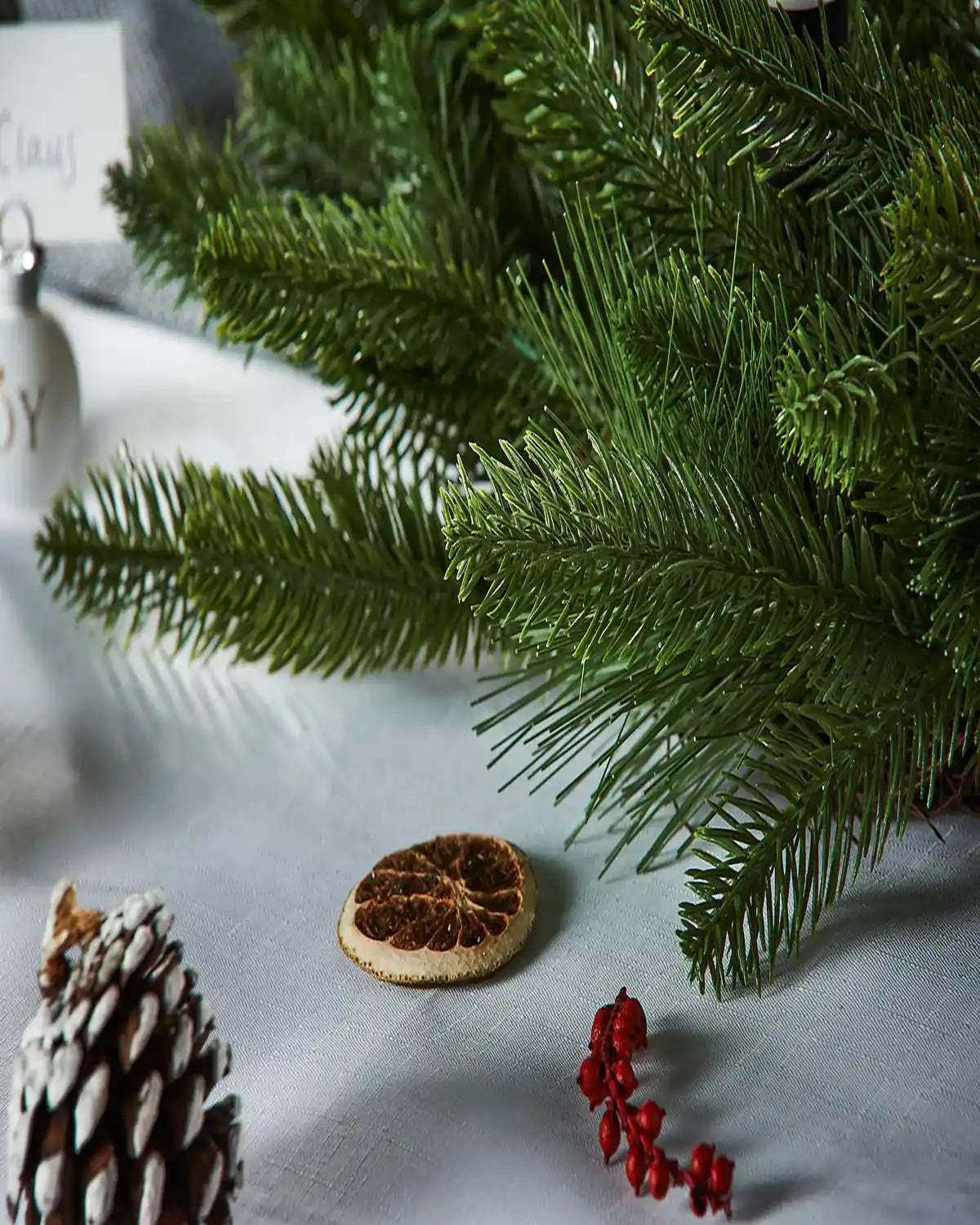 Close-up of a Christmas wreath branch with pine cones and berries on a white surface.