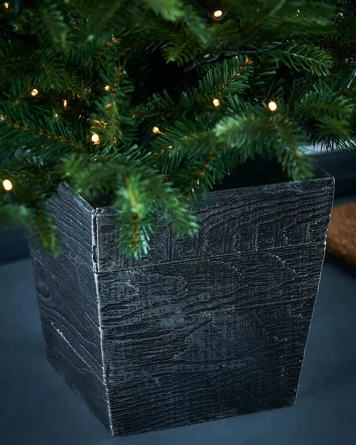 Close-up of a Decorated Pre-Lit Grand Fir Potted Christmas Tree with single lit warm white lights in a textured black pot 