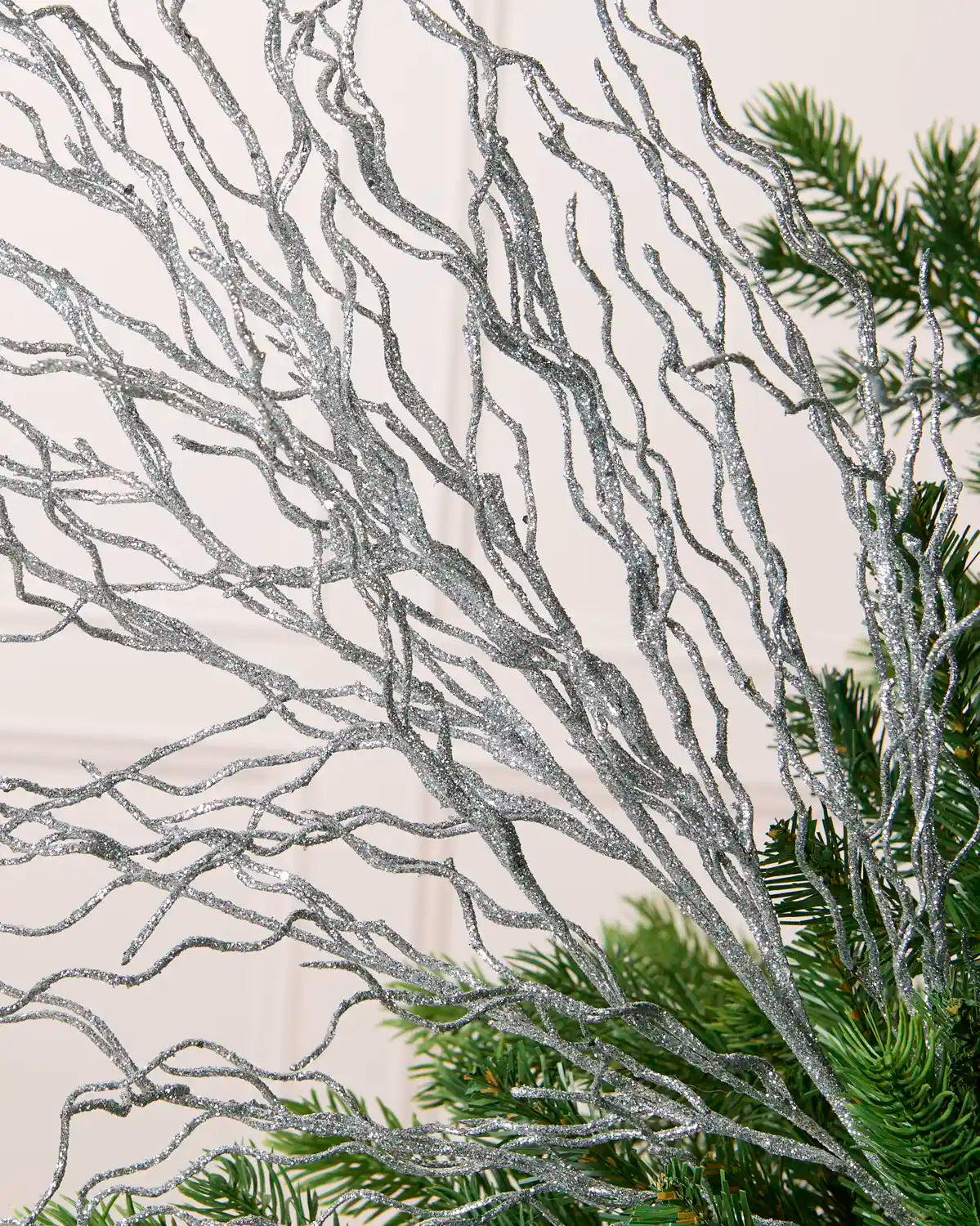 Close-up of a Glitter Twig Tree Topper with silver glittered branches nestled among green Christmas tree branches