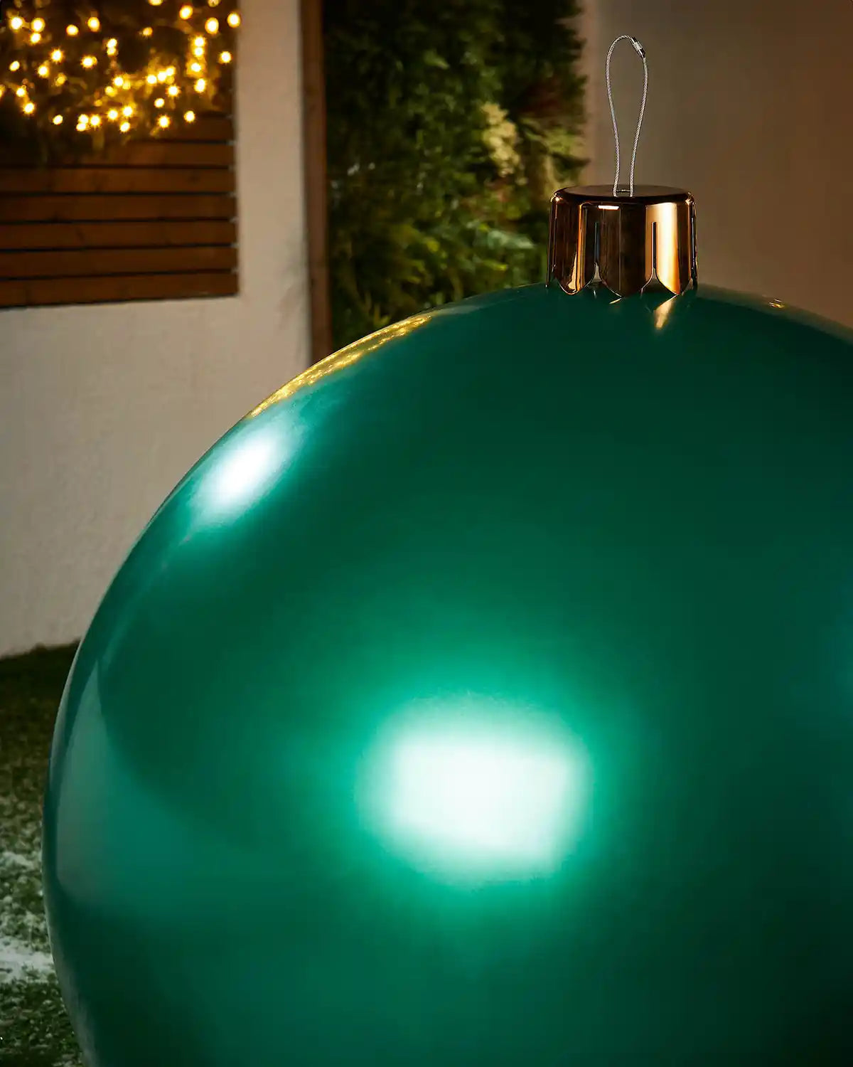Close-up of a Large green Christmas inflatable bauble with gold cap against a blurred indoor background
