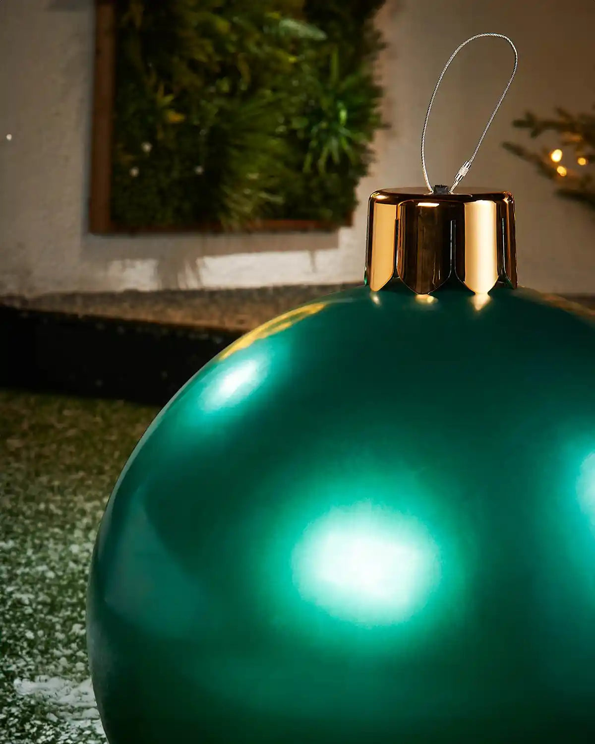 Close-up of a Medium green Christmas inflatable bauble with gold cap against a blurred indoor background

