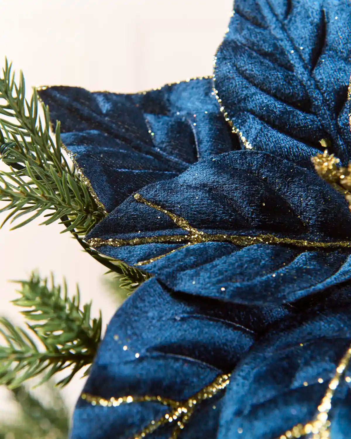 Close-up of a Navy glitter artificial poinsettia flower, highlighting the layered velvet-like petals and gold glitter detailing along the edges and veins
