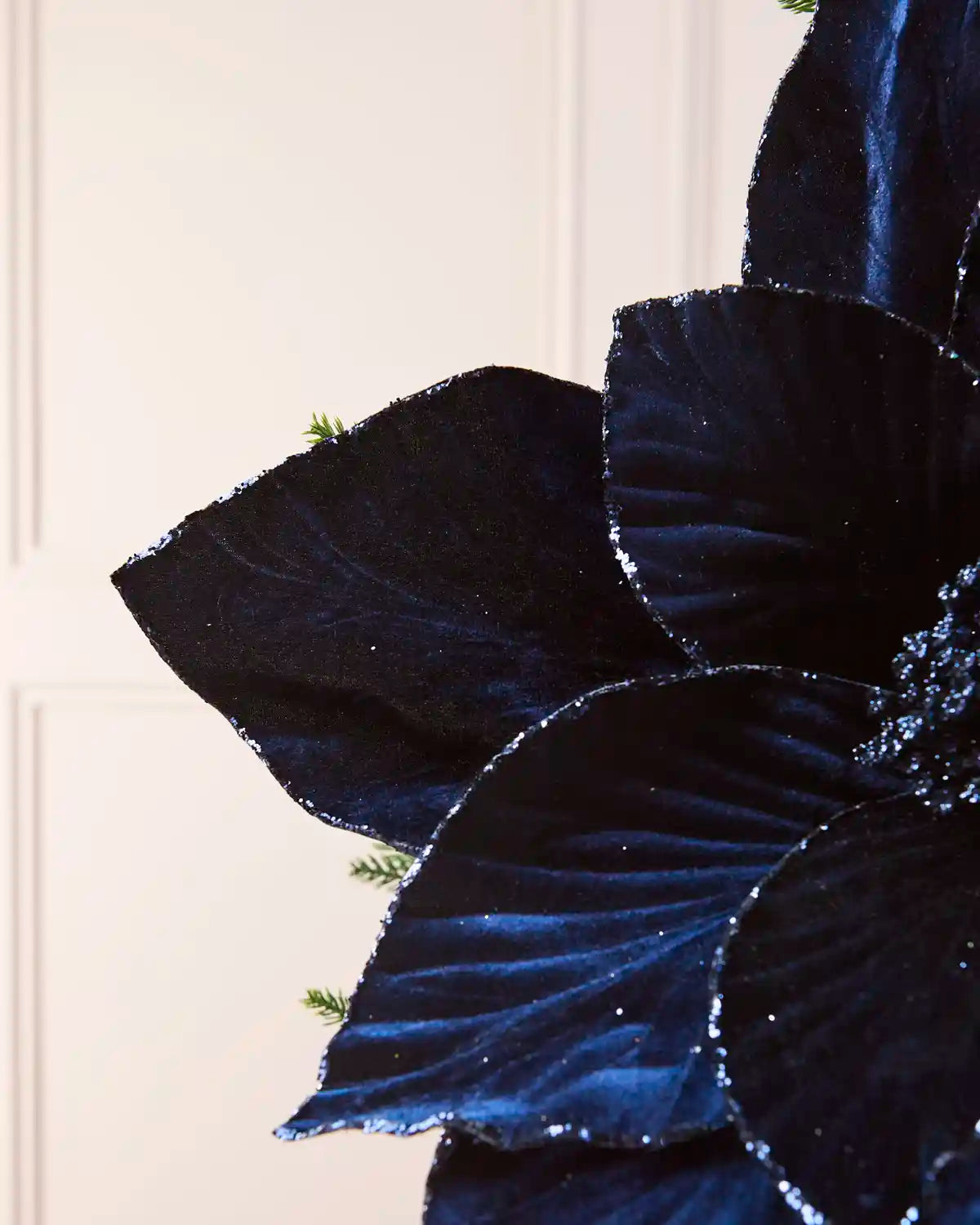 Close-up of a Navy velvet artificial poinsettia, highlighting its soft texture, detailed petal veining and glittered edges.
